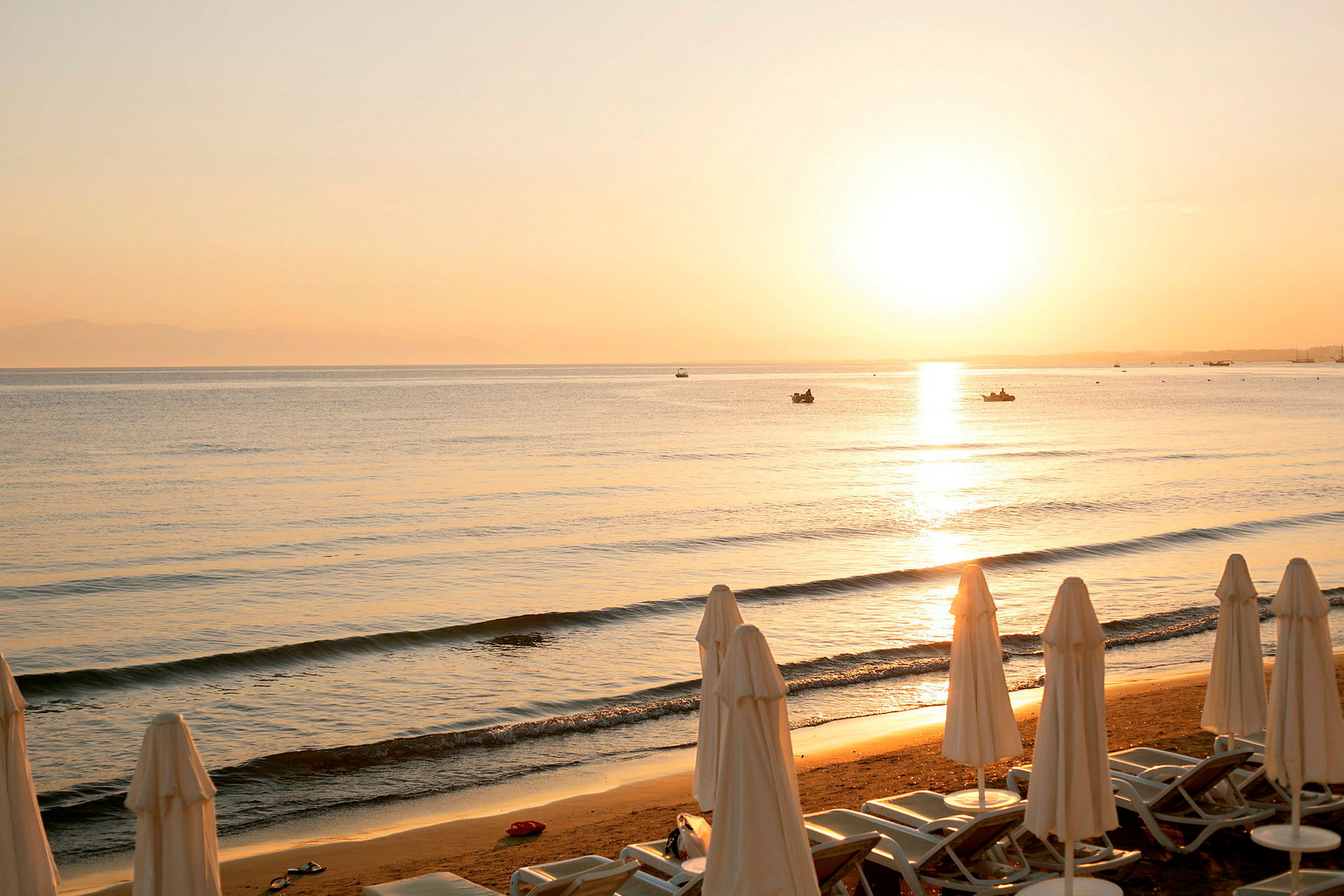 Strand ved solnedgang med solsenger og parasoller. (AI-generert tekst)