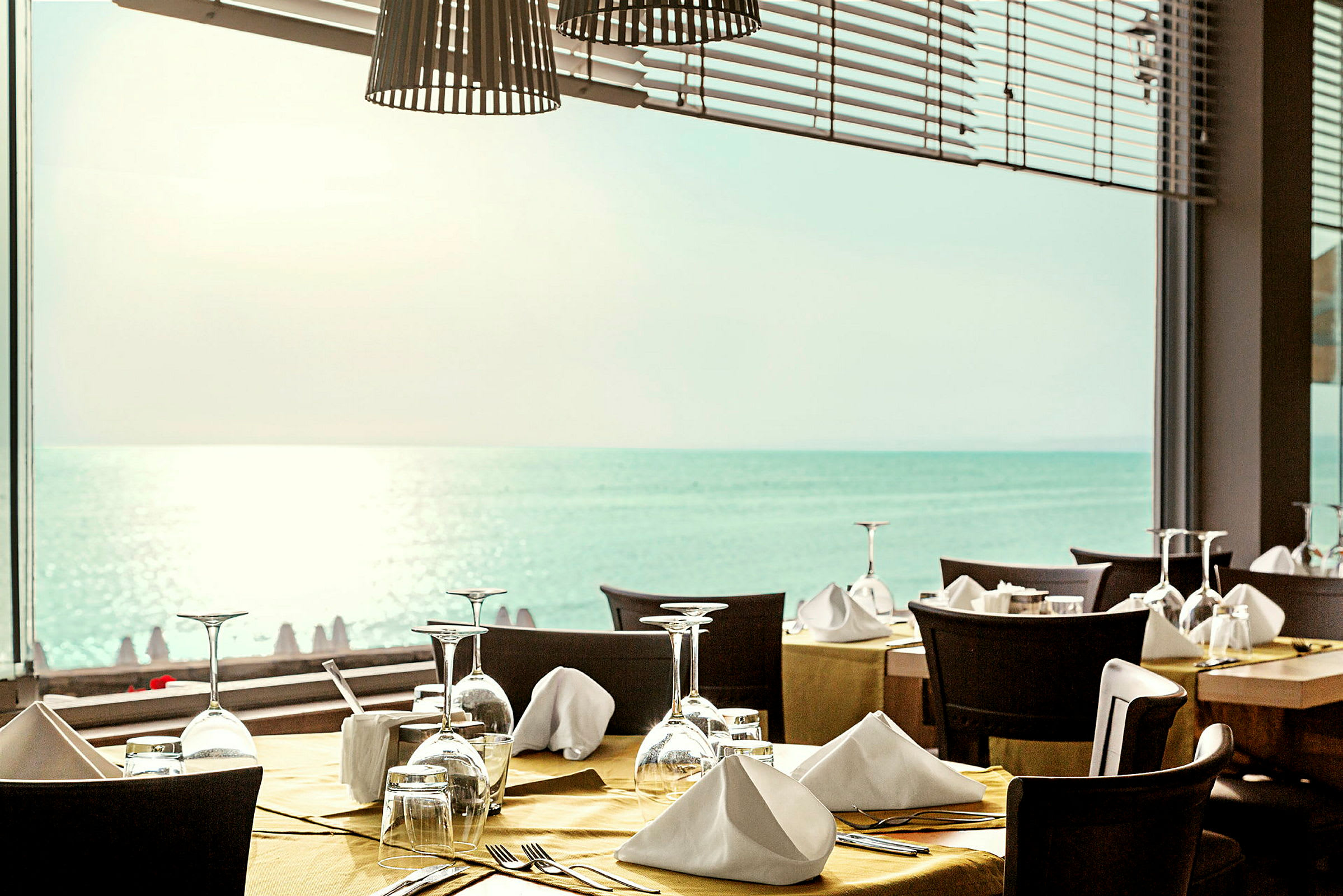 Restaurant med dekkede bord foran et vindu som har utsikt over havet. (AI-generert tekst)