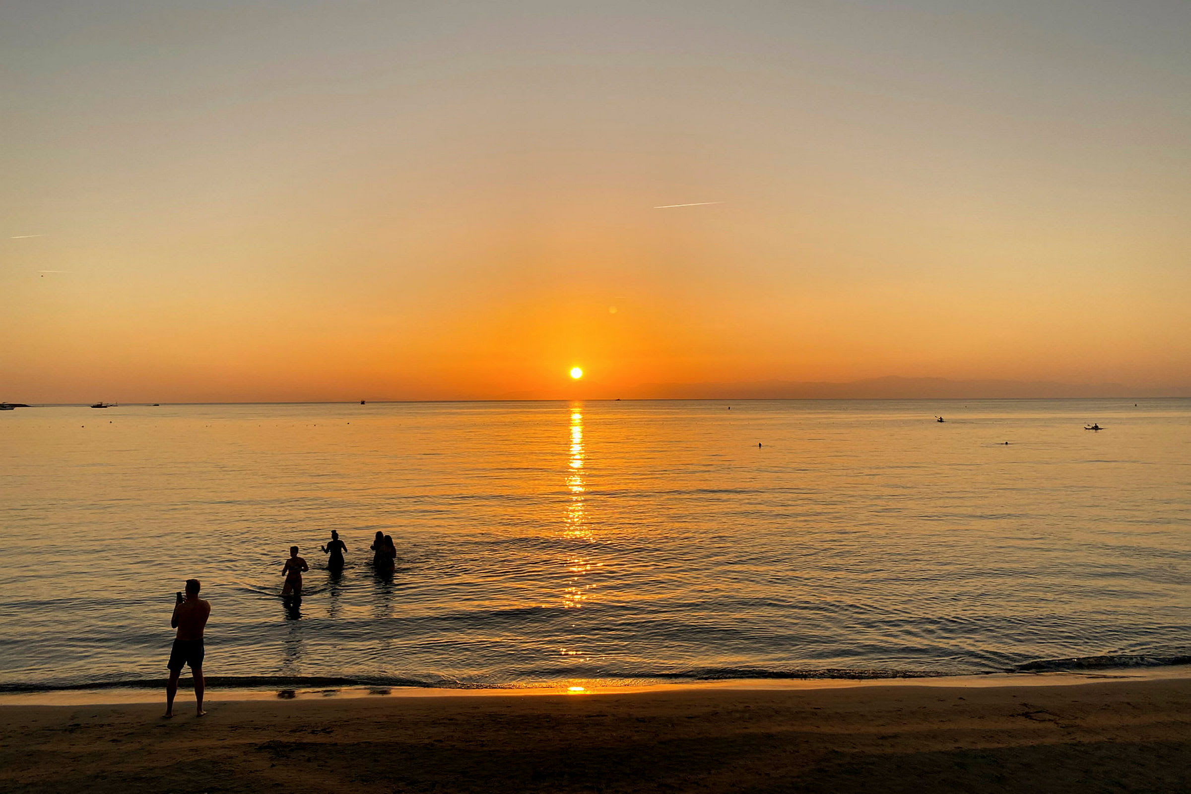 En strand ved solnedgangen med mennesker i vannet. (AI-generert tekst)