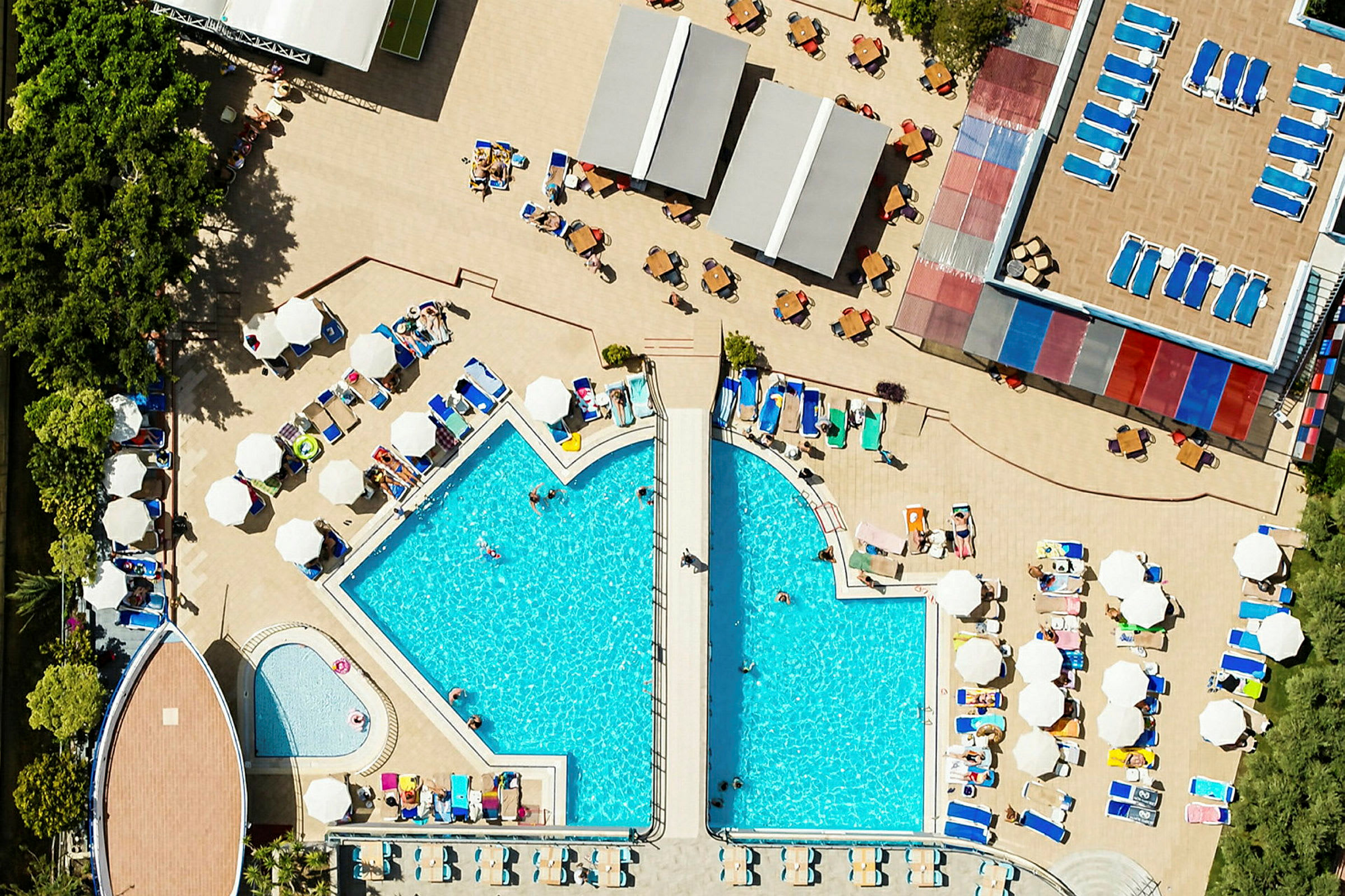 Et oversiktsbilde av et hotellbasseng med omkringliggende solsenger og parasoller. (AI-generert tekst)