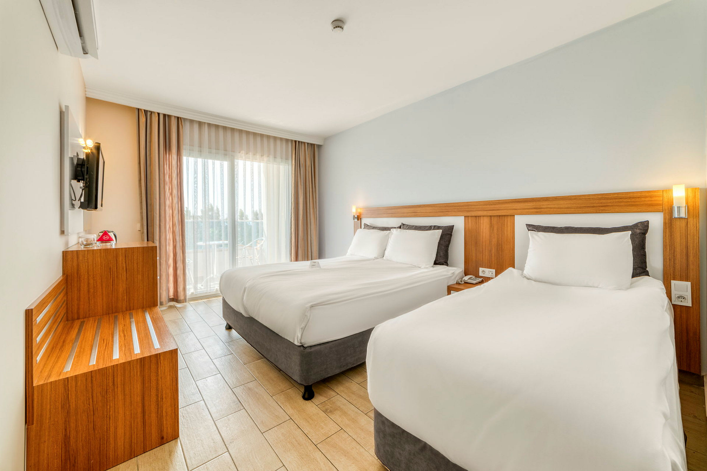 Moderne hotellrom med to senger, lyse farger og store vinduer. (AI-generert tekst)