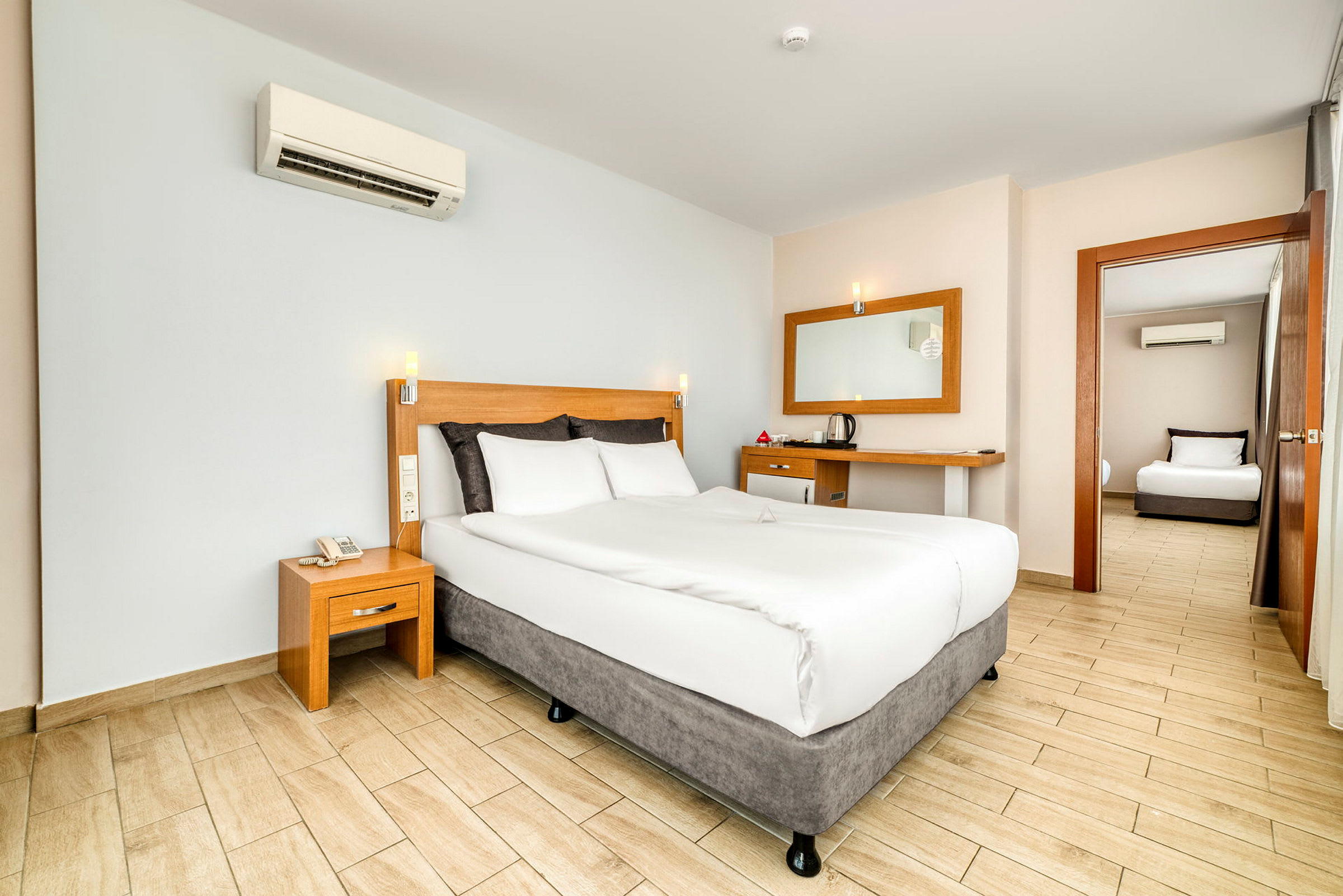 Hotellrom med en dobbeltseng, nattbord og skrivebord samt en dør som leder til et annet rom. (AI-generert tekst)