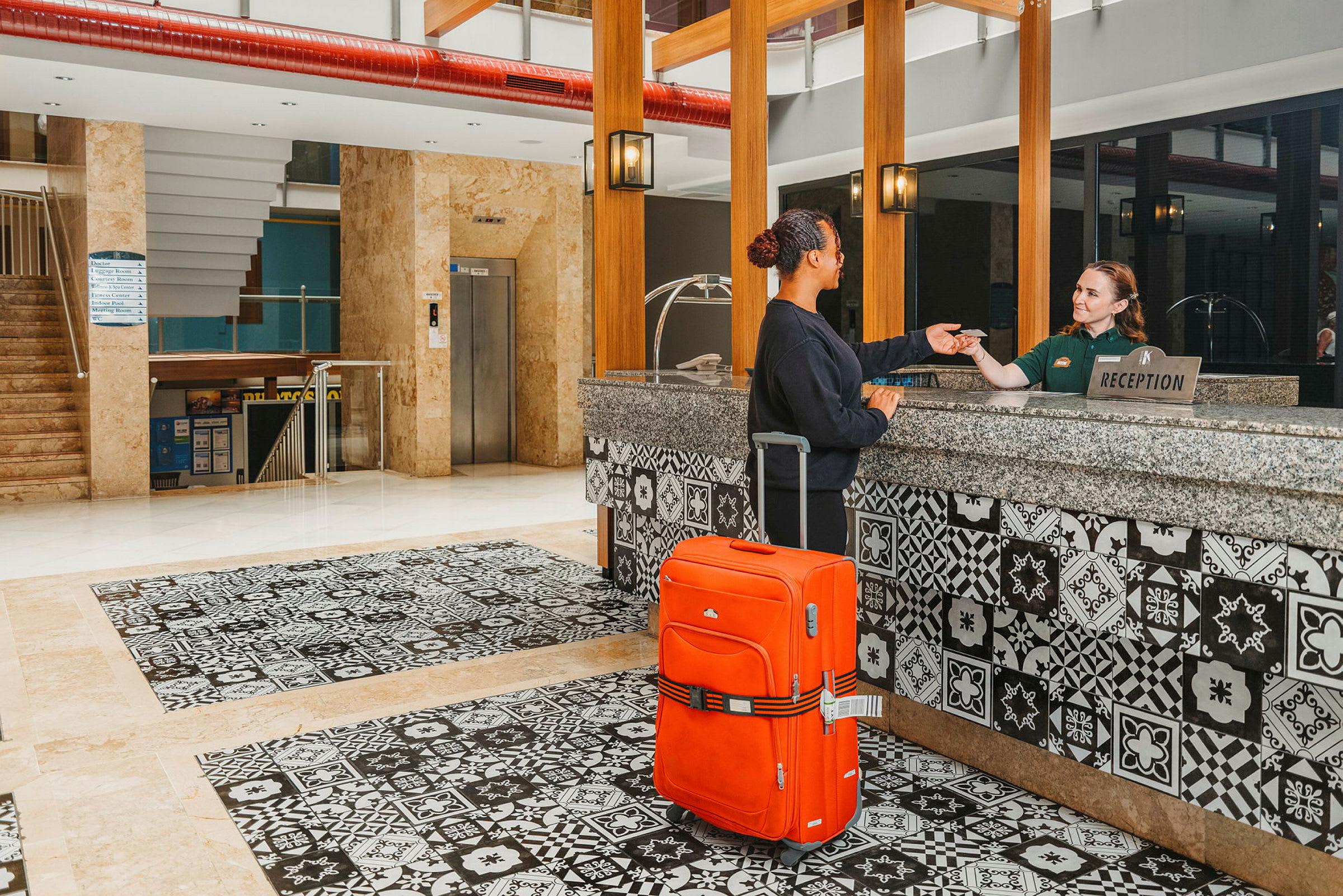 En person ved en hotellresepsjon med en oransje koffert. (AI-generert tekst)