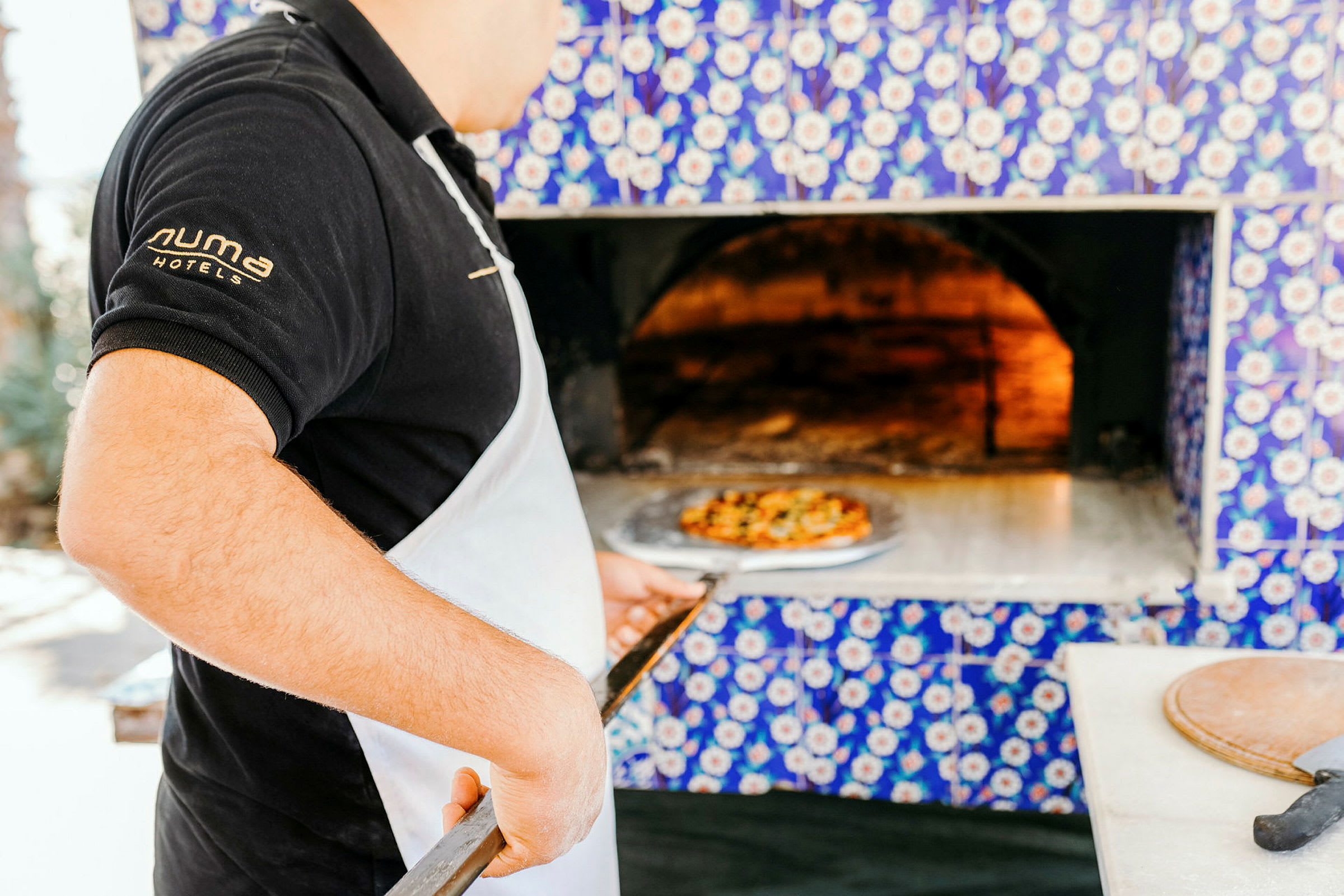 Person holder en pizzaspade foran en vedovn. (AI-generert tekst)