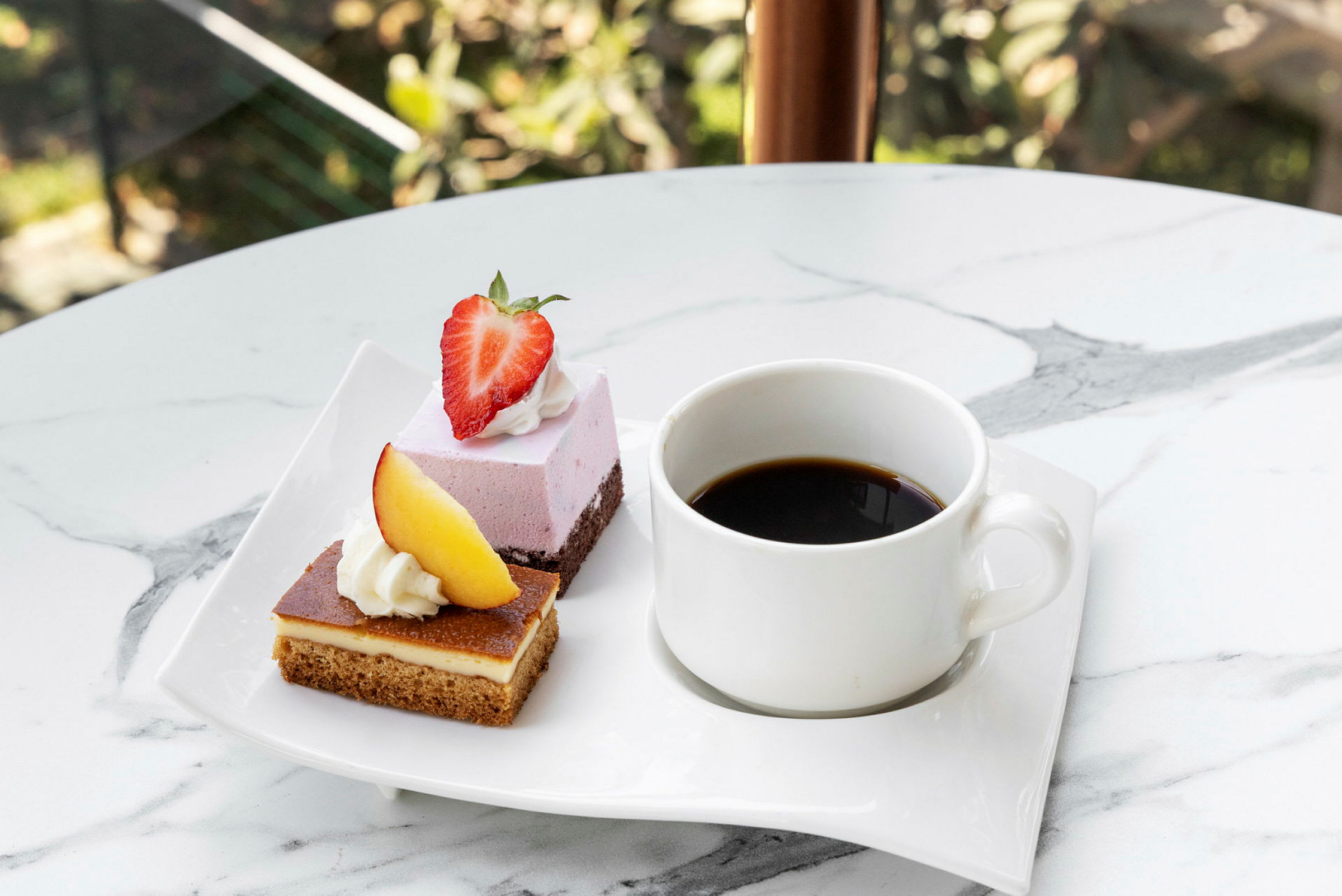 En hvit tallerken med to desserter, en toppet med et jordbær og en med et stykke fersken, samt en kopp svart kaffe. (AI-generert tekst)