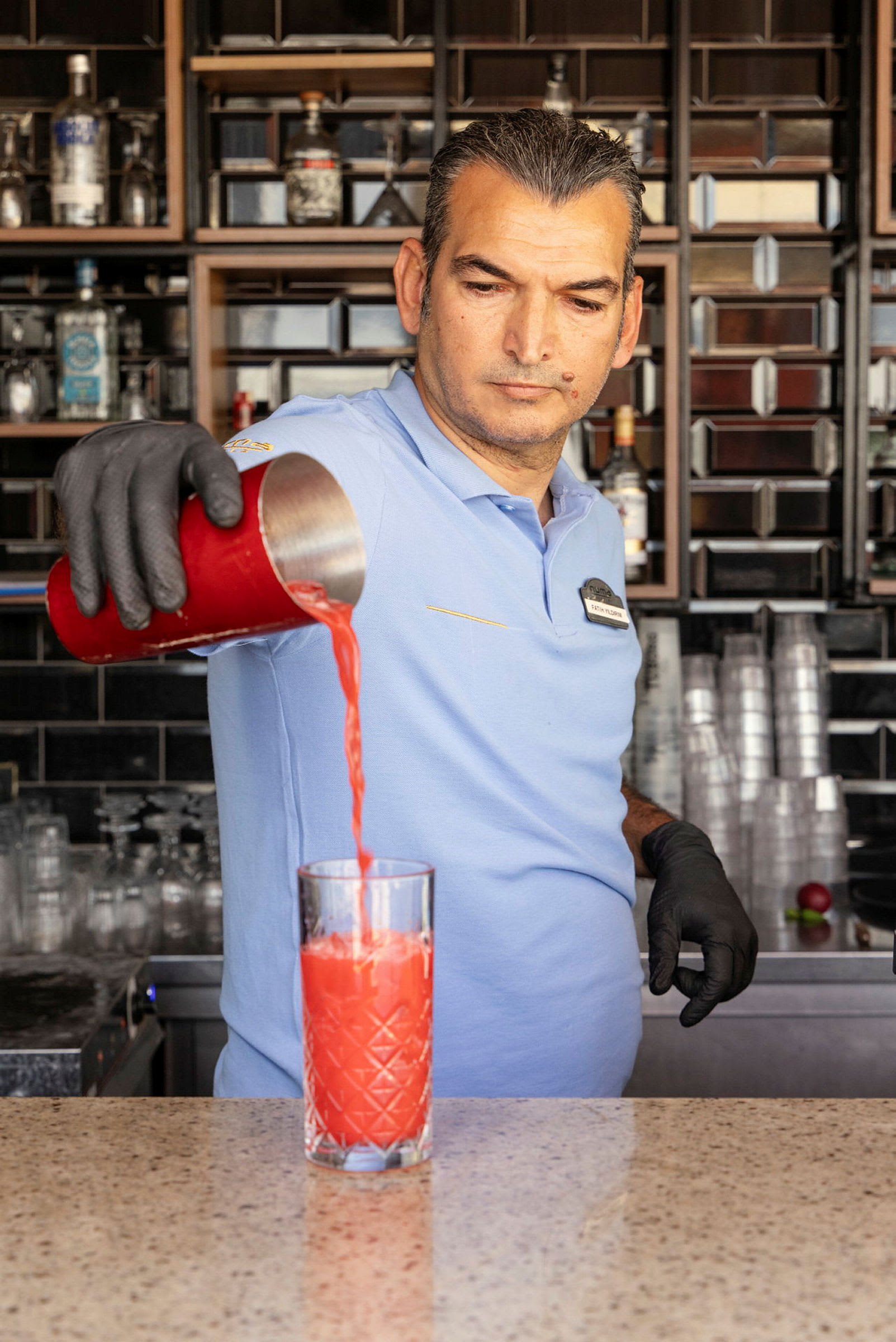 En bartender heller en rød drikk fra en shaker i et glass. (AI-generert tekst)