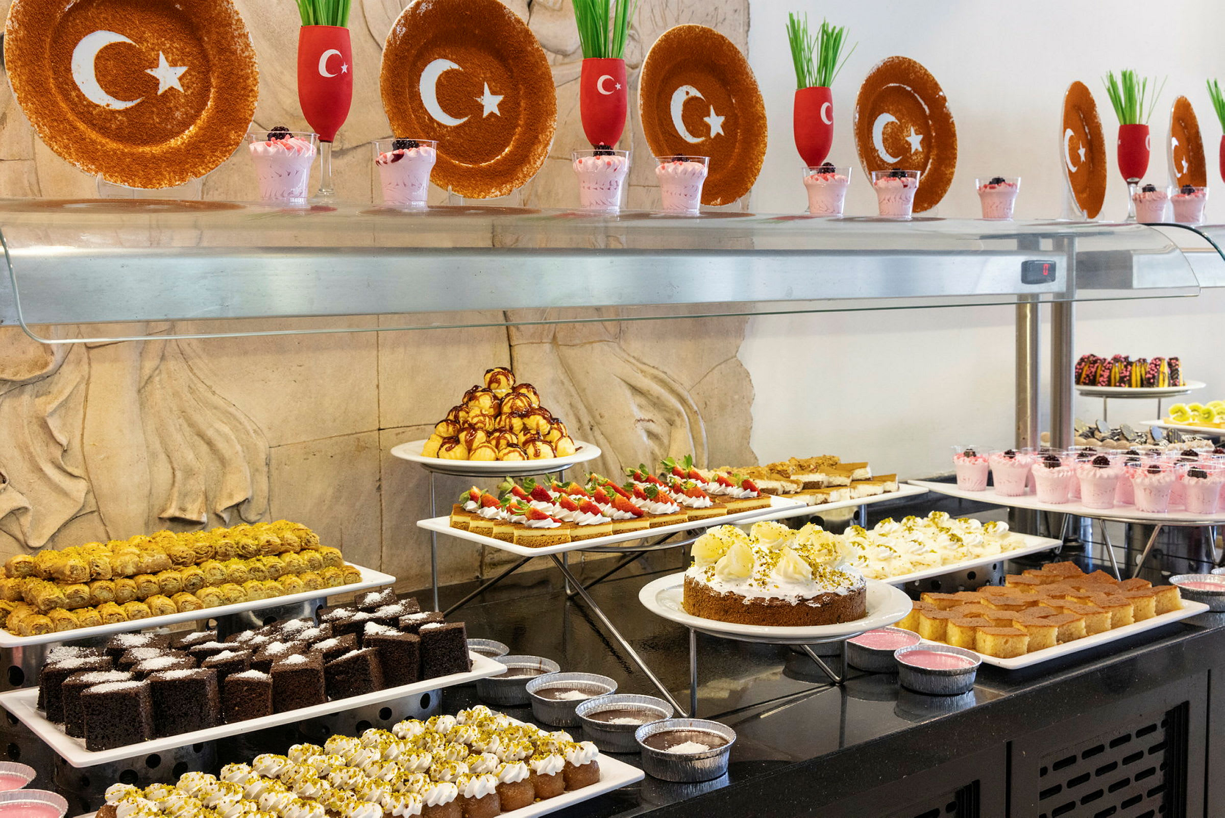 Bilde av en dessertbuffet med forskjellige bakverk og desserter, dekorert med tallerkener og glass med tyrkiske flaggsymboler. (AI-generert tekst)