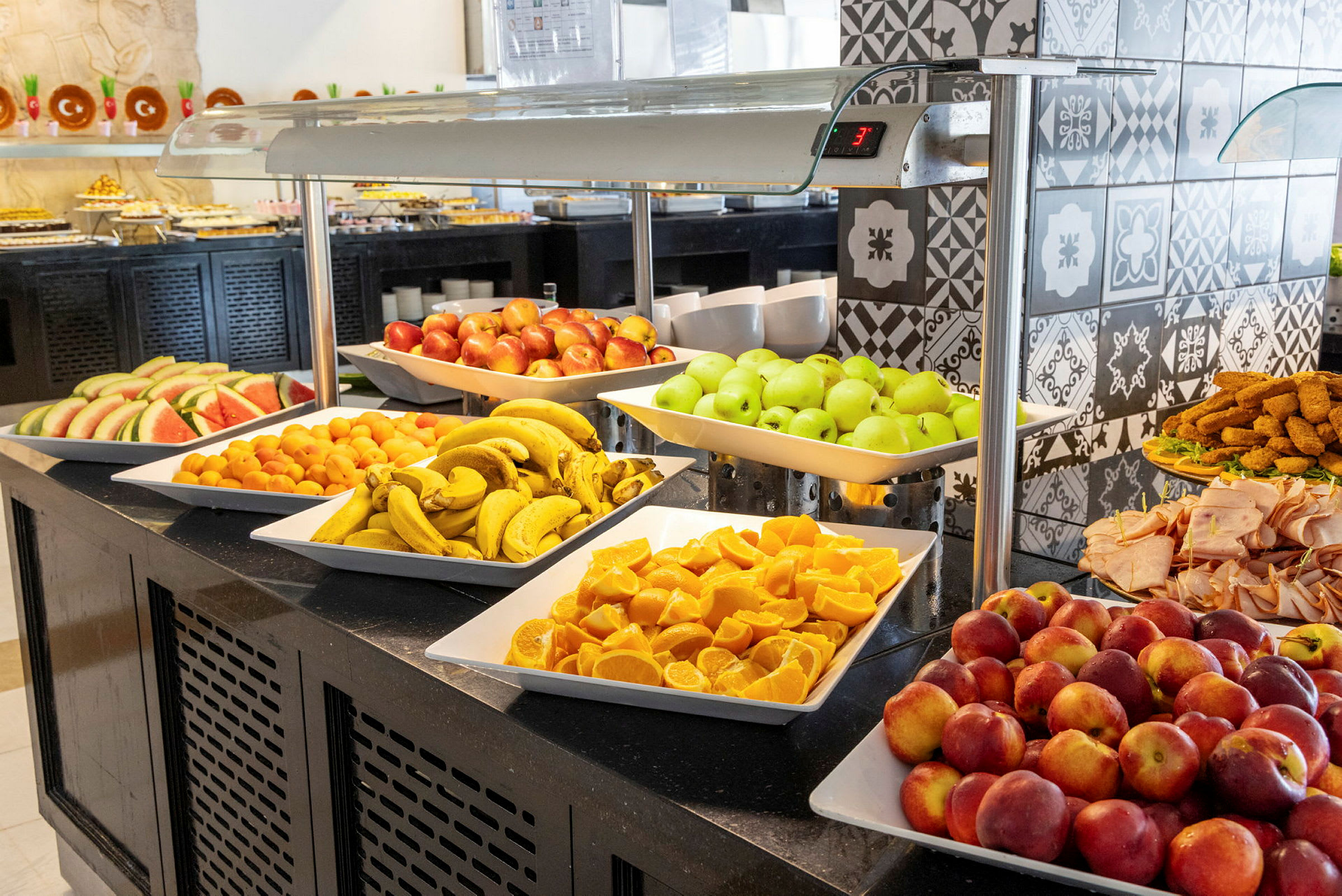 En buffé med forskjellige frukter som bananer, epler, appelsiner og vannmelon samt pålegg og andre tilbehør. (AI-generert tekst)