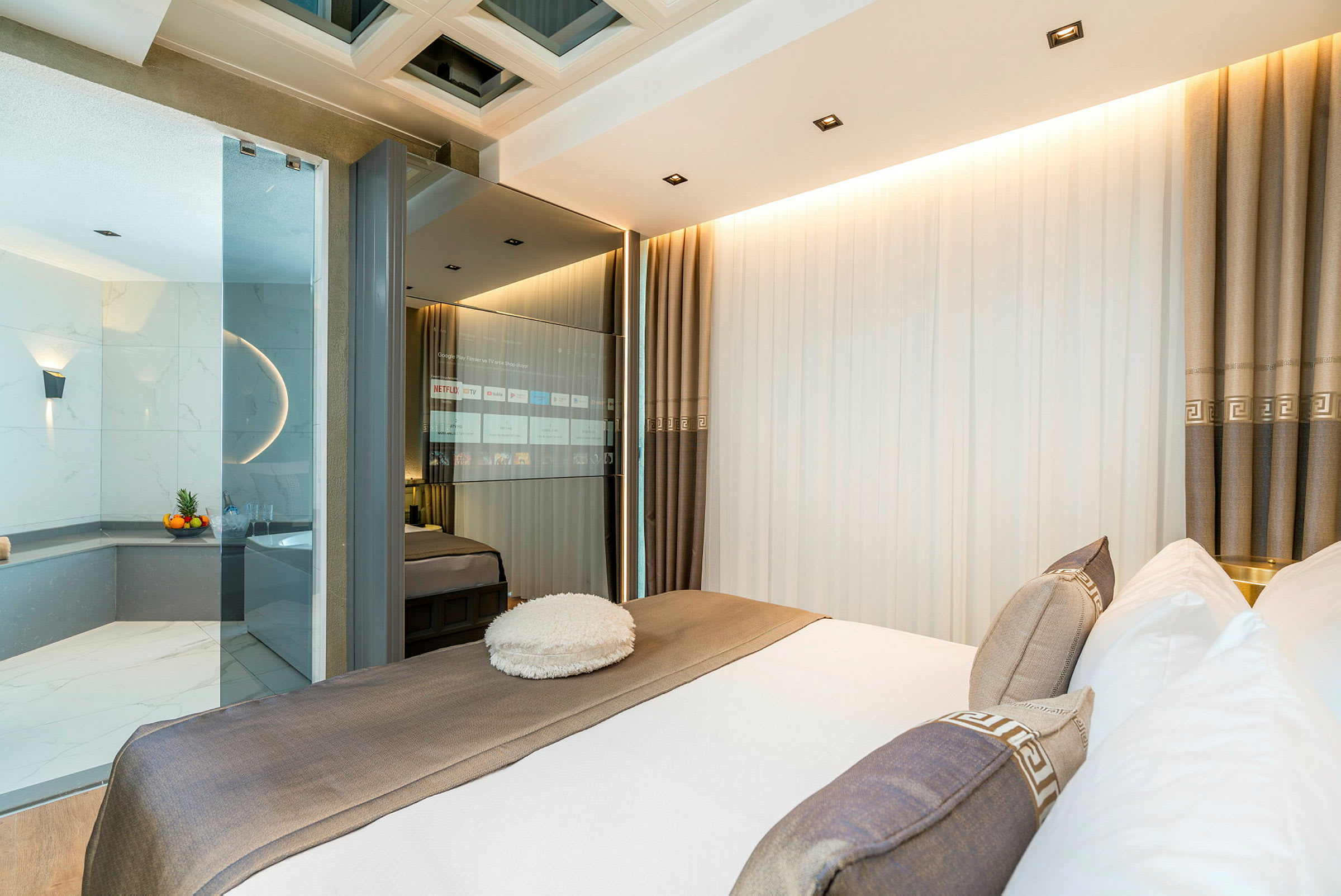 Moderne hotellrom med en stor seng, glassvegg og utsikt mot et marmordekket badekar. (AI-generert tekst)
