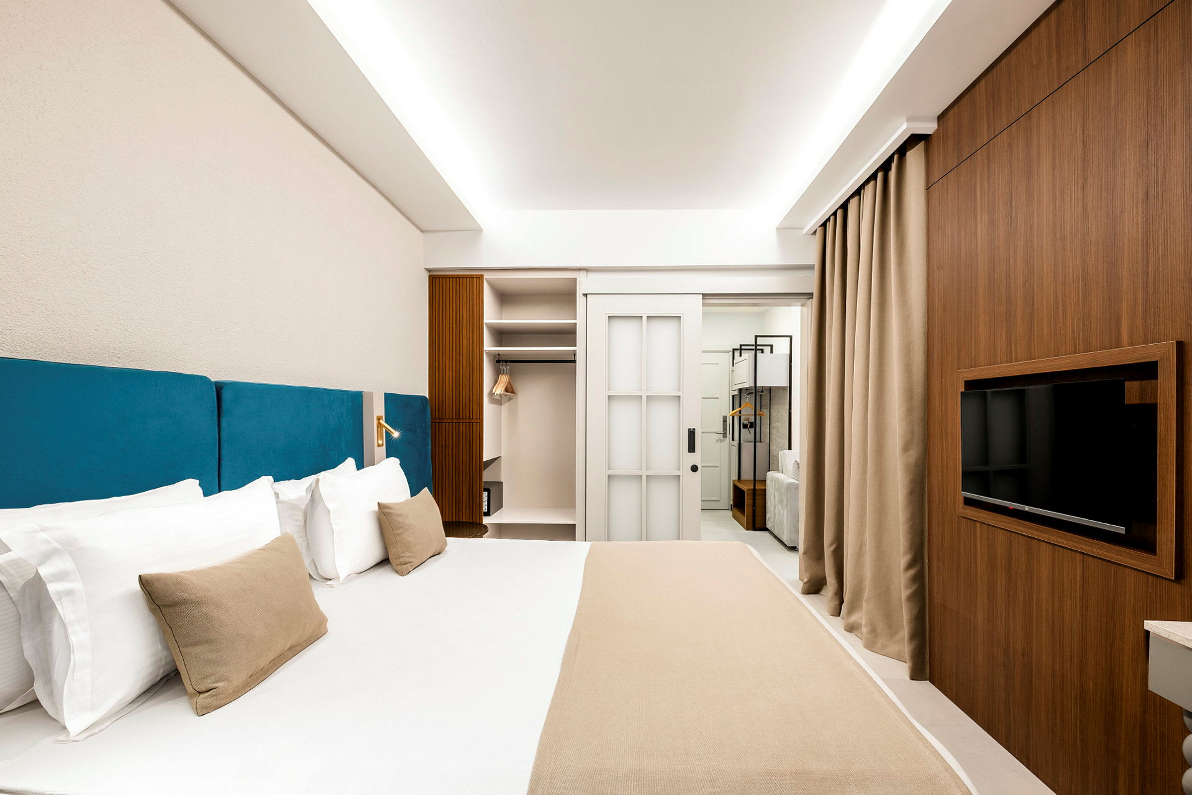Hotellrom med en stor seng med blå sengegavl, en garderobe, TV og moderne innredning. (AI-generert tekst)