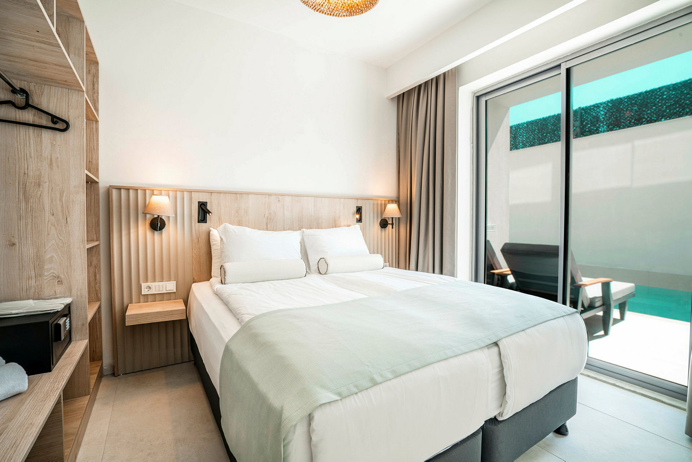 Et hotellrom med en dobbeltseng, skuffer og en balkong med utsikt mot et basseng. (AI-generert tekst)