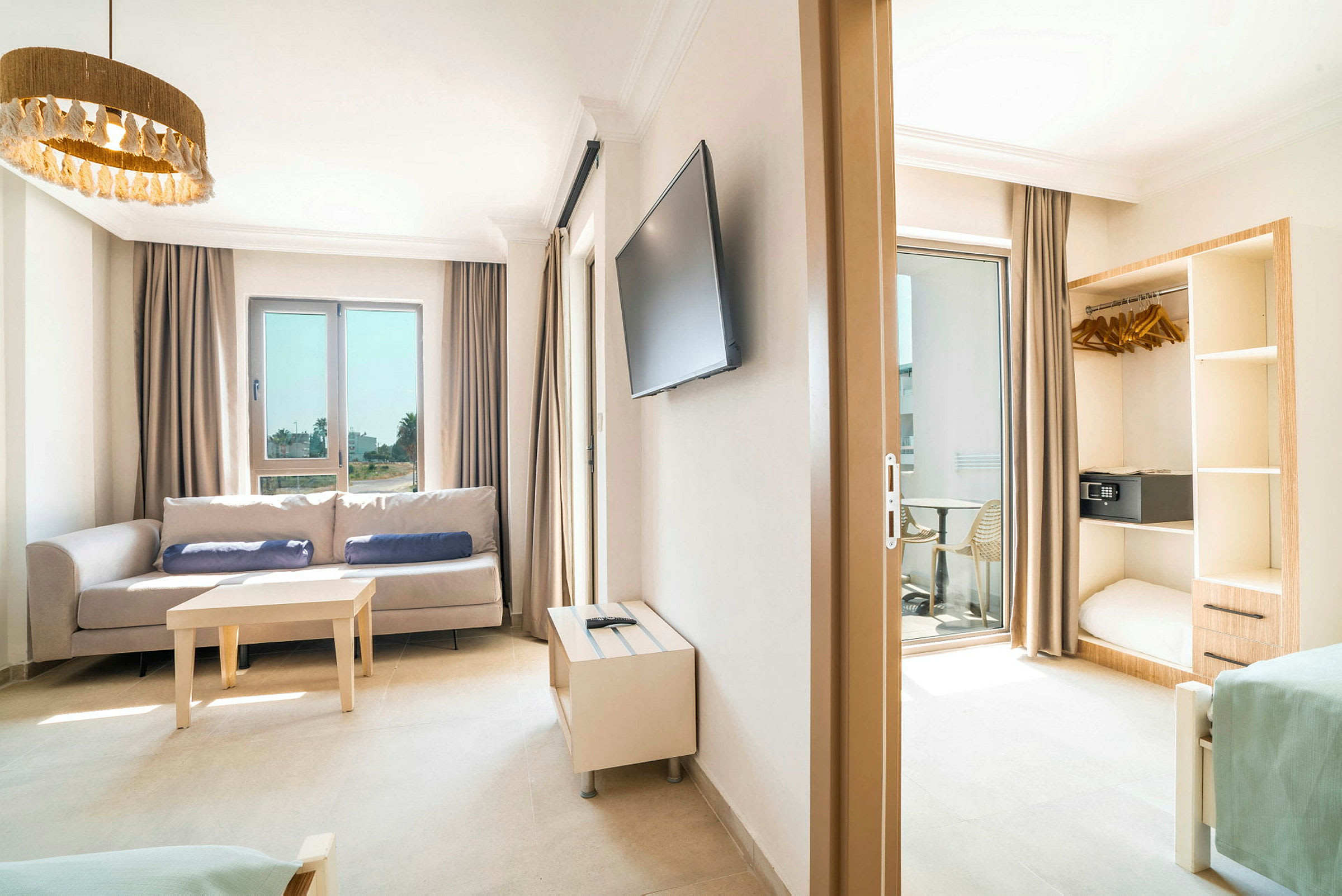 Bilde av et lyst hotellrom med sofa, bord, TV og åpen garderobe. (AI-generert tekst)