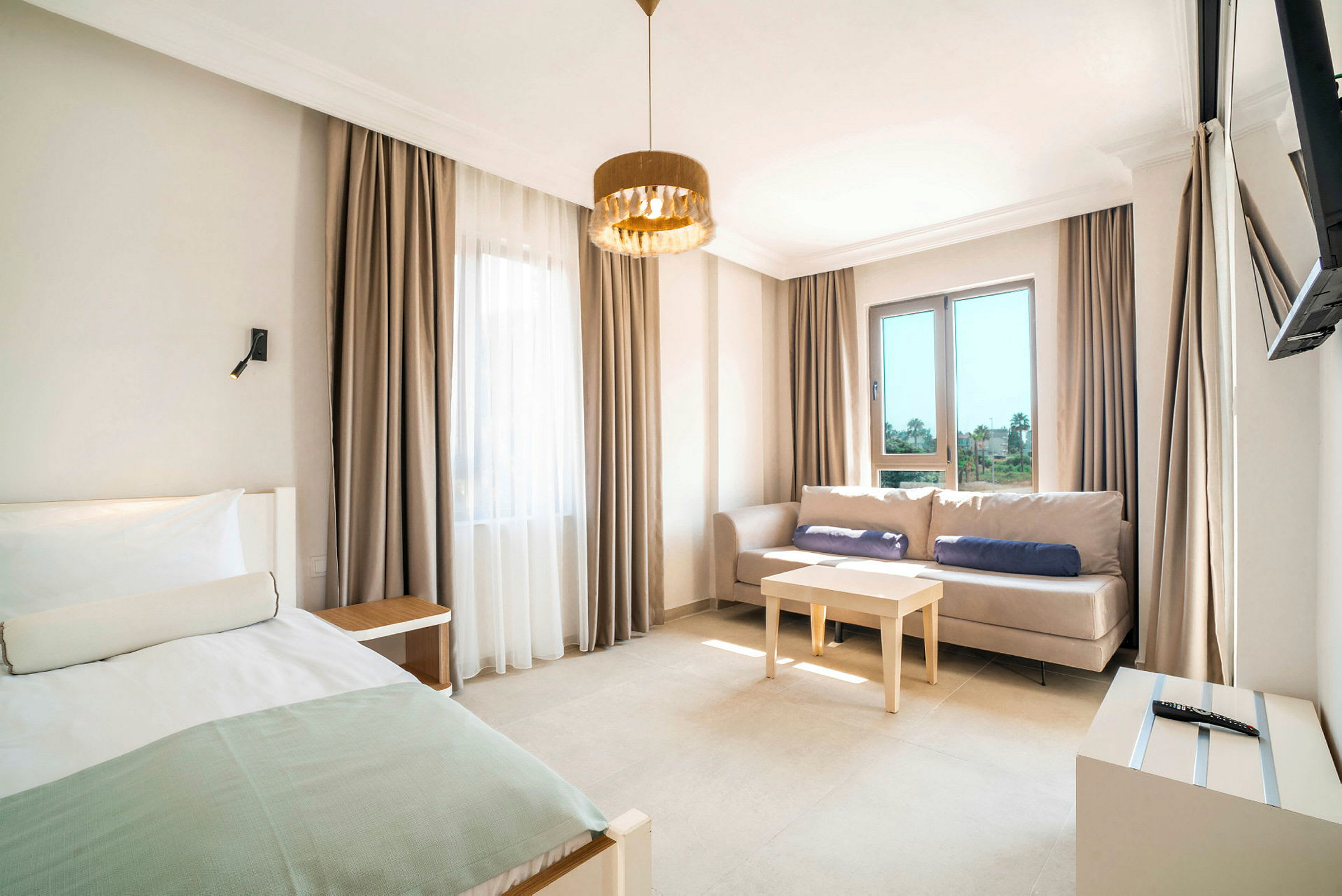 Et hotellrom med en seng, en sofa, et bord og store vinduer. (AI-generert tekst)