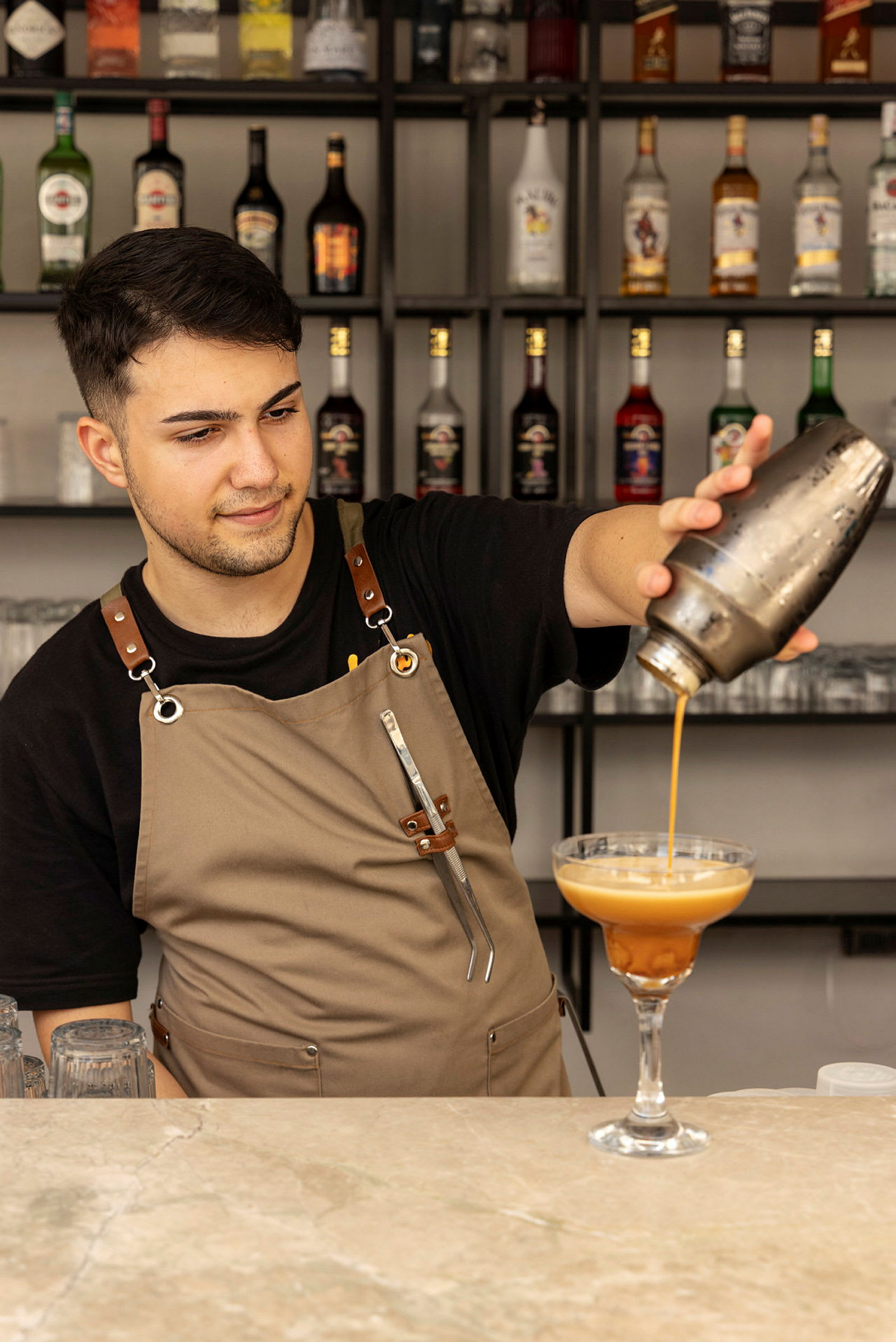 En bartender heller en drink fra en shaker i et cocktailglass. (AI-generert tekst)