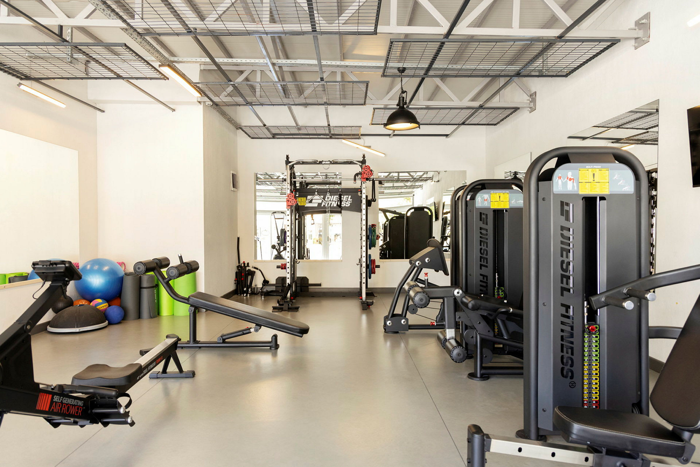 Et treningsstudio med ulike treningsmaskiner, treningsbenker og tilbehør som medisinballer og fitnessballer. (AI-generert tekst)