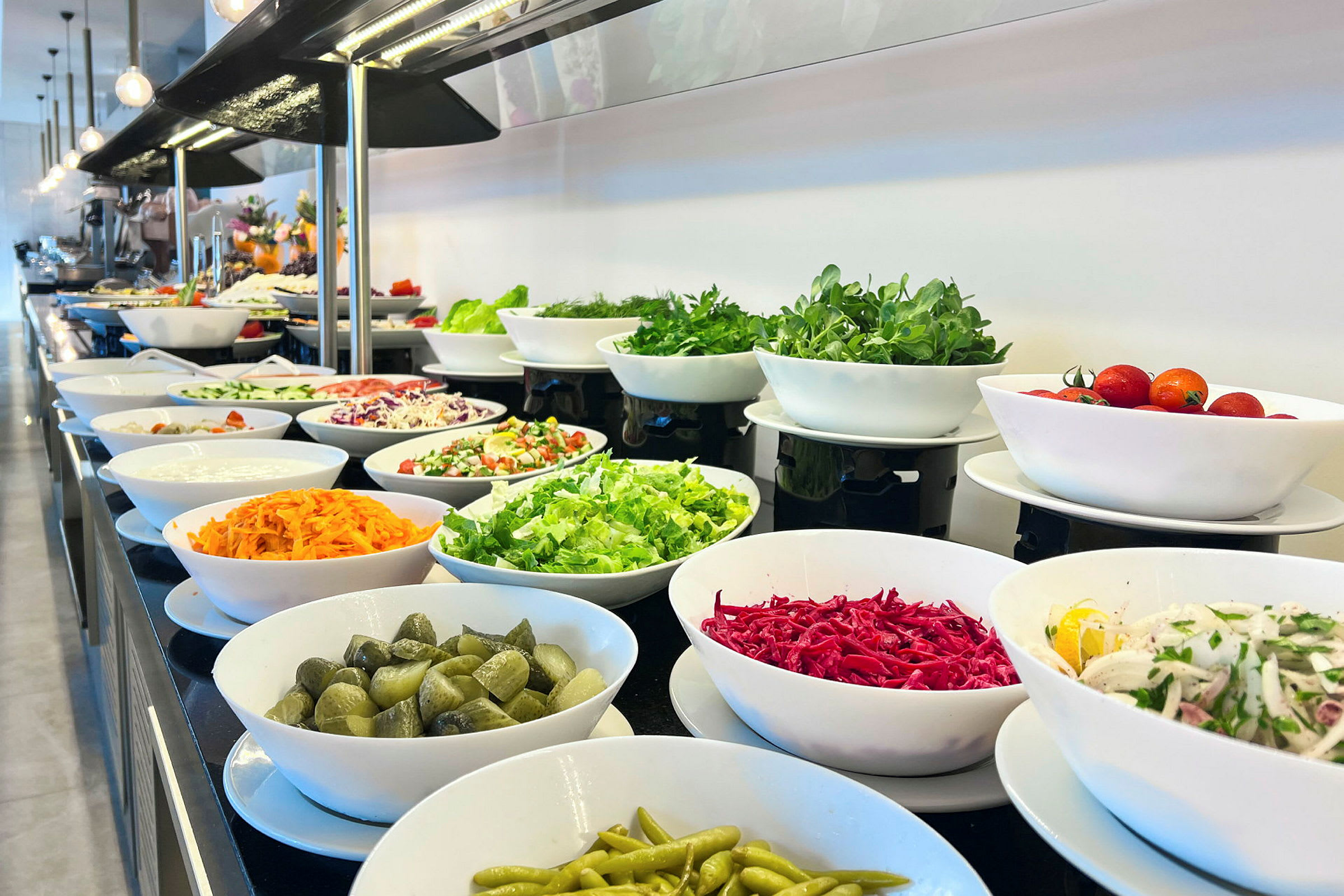 En buffet med salat og grønnsaker i hvite skåler. (AI-generert tekst)
