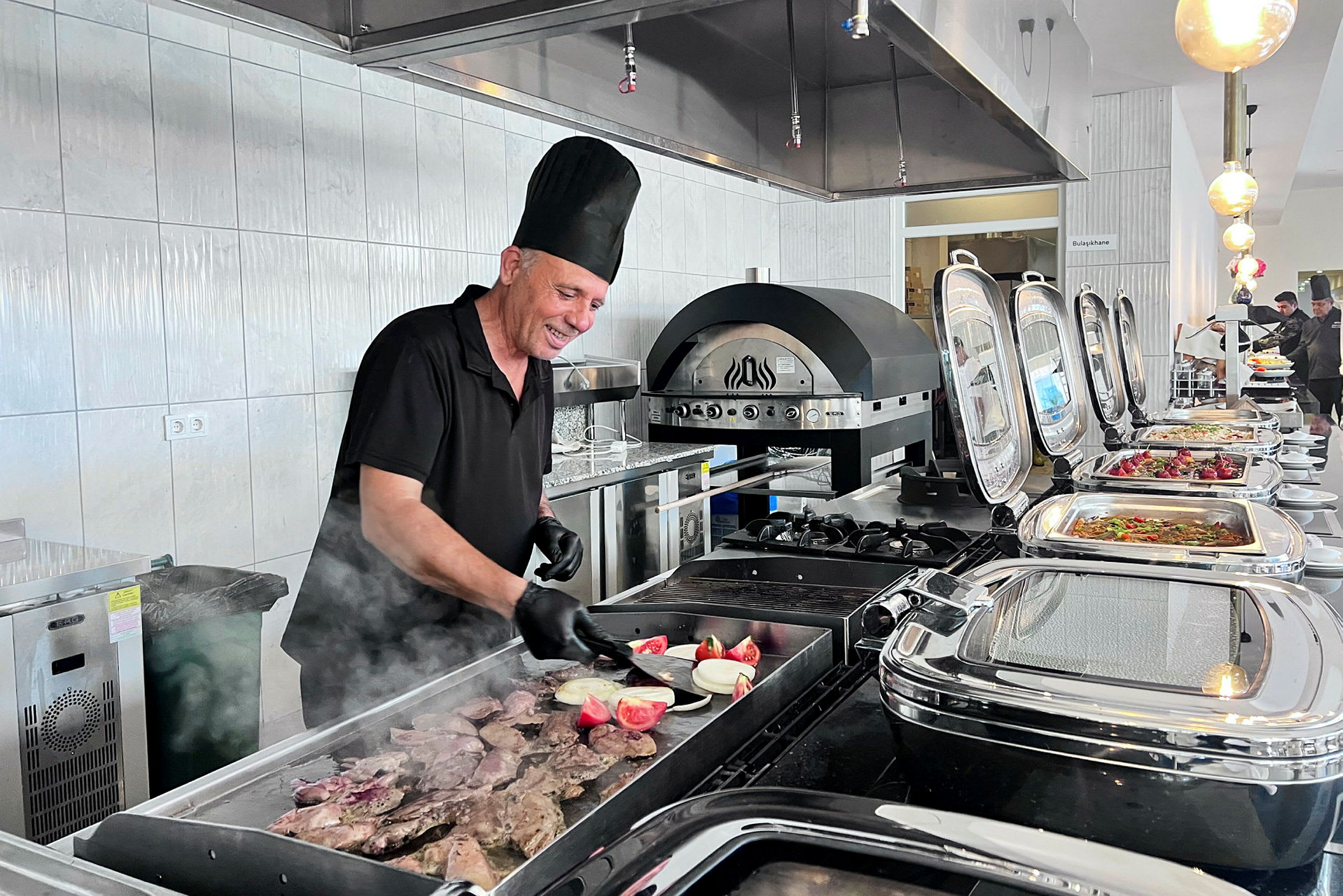 En kokk lager mat på en grill i et buffémiljø. (AI-generert tekst)