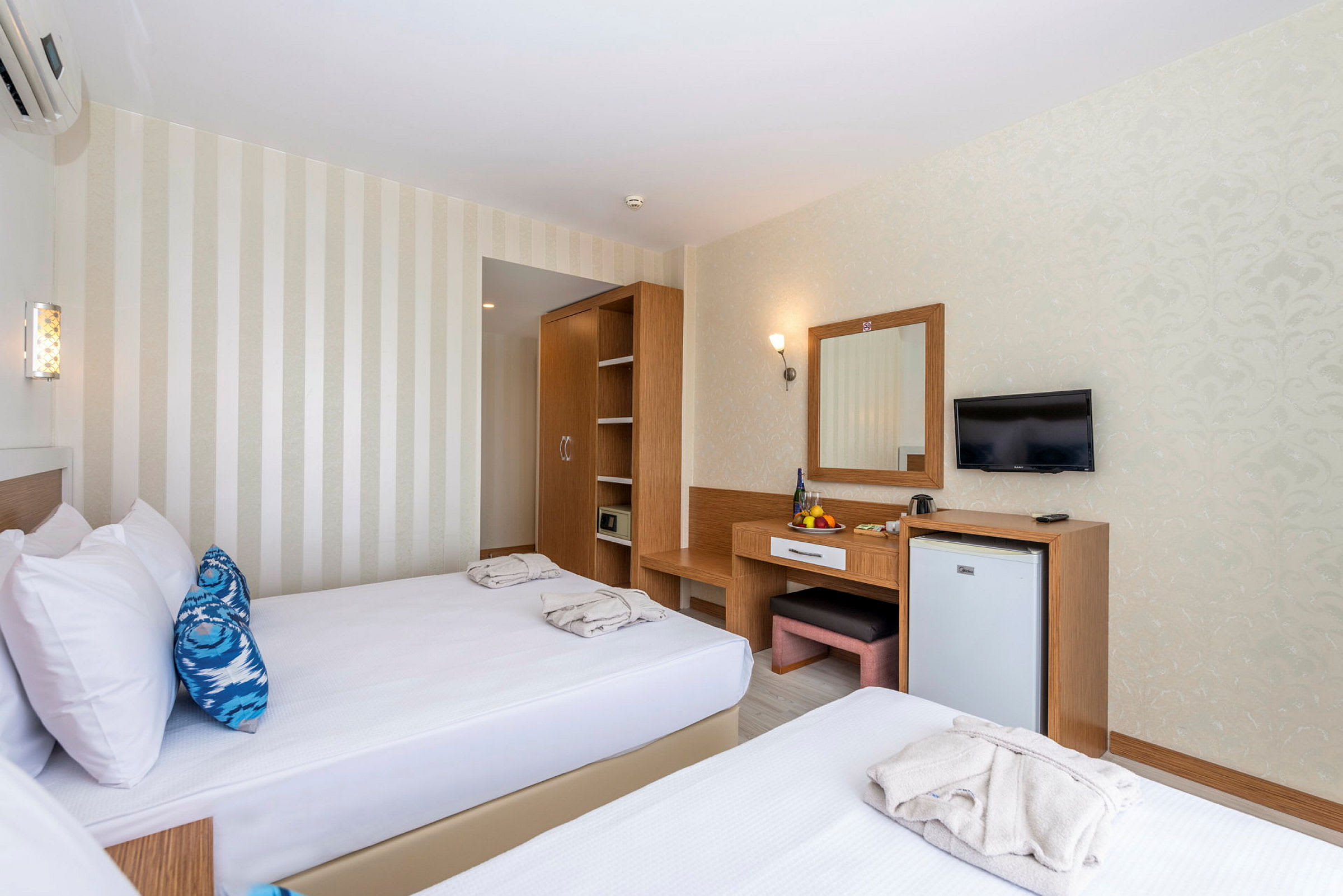 Hotellrom med to enkeltsenger, et skap, et skrivebord med speil og en veggmontert TV. (AI-generert tekst)