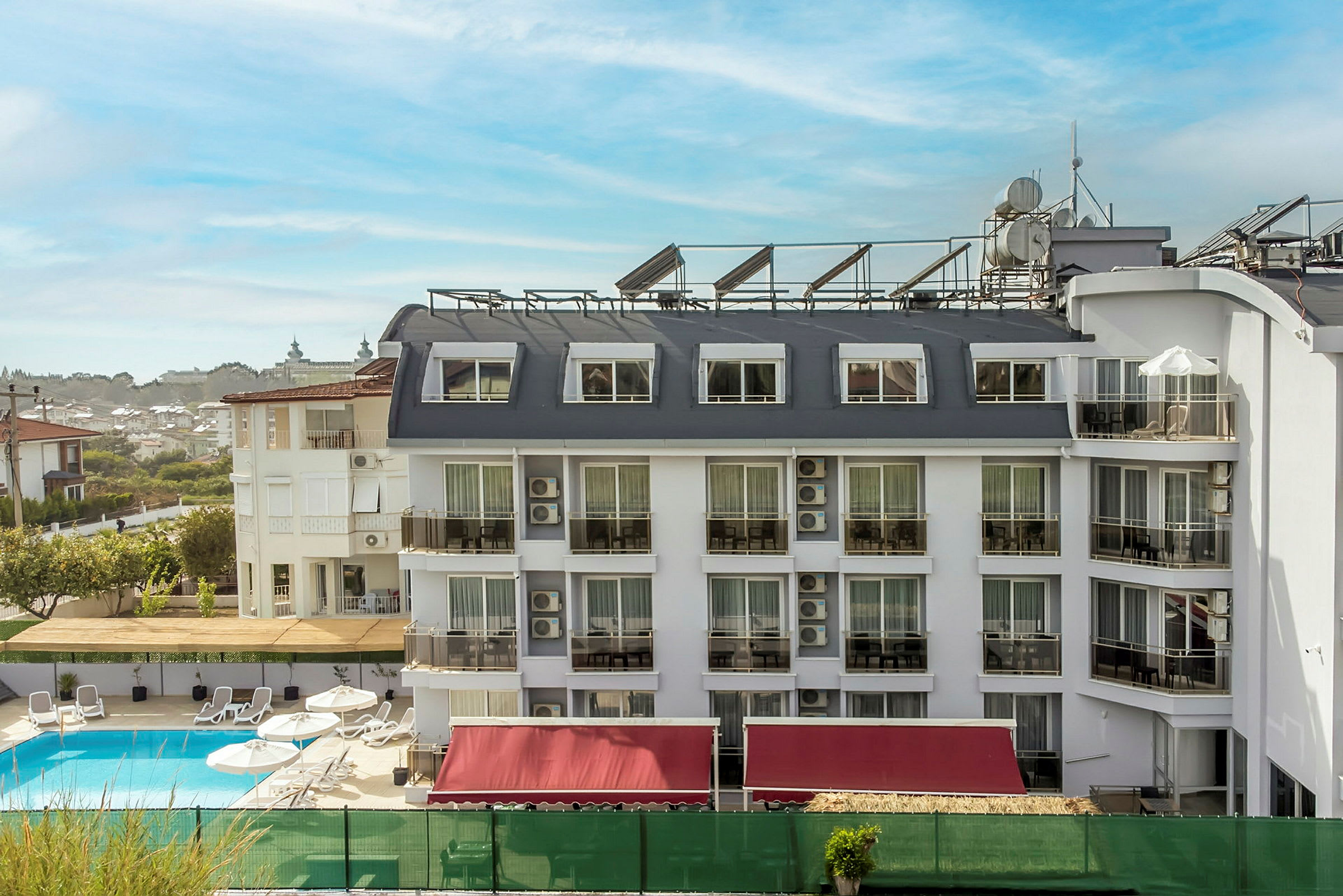 Et hotell med hvit fasade og flere vinduer og balkonger, et basseng foran bygningen. (AI-generert tekst)