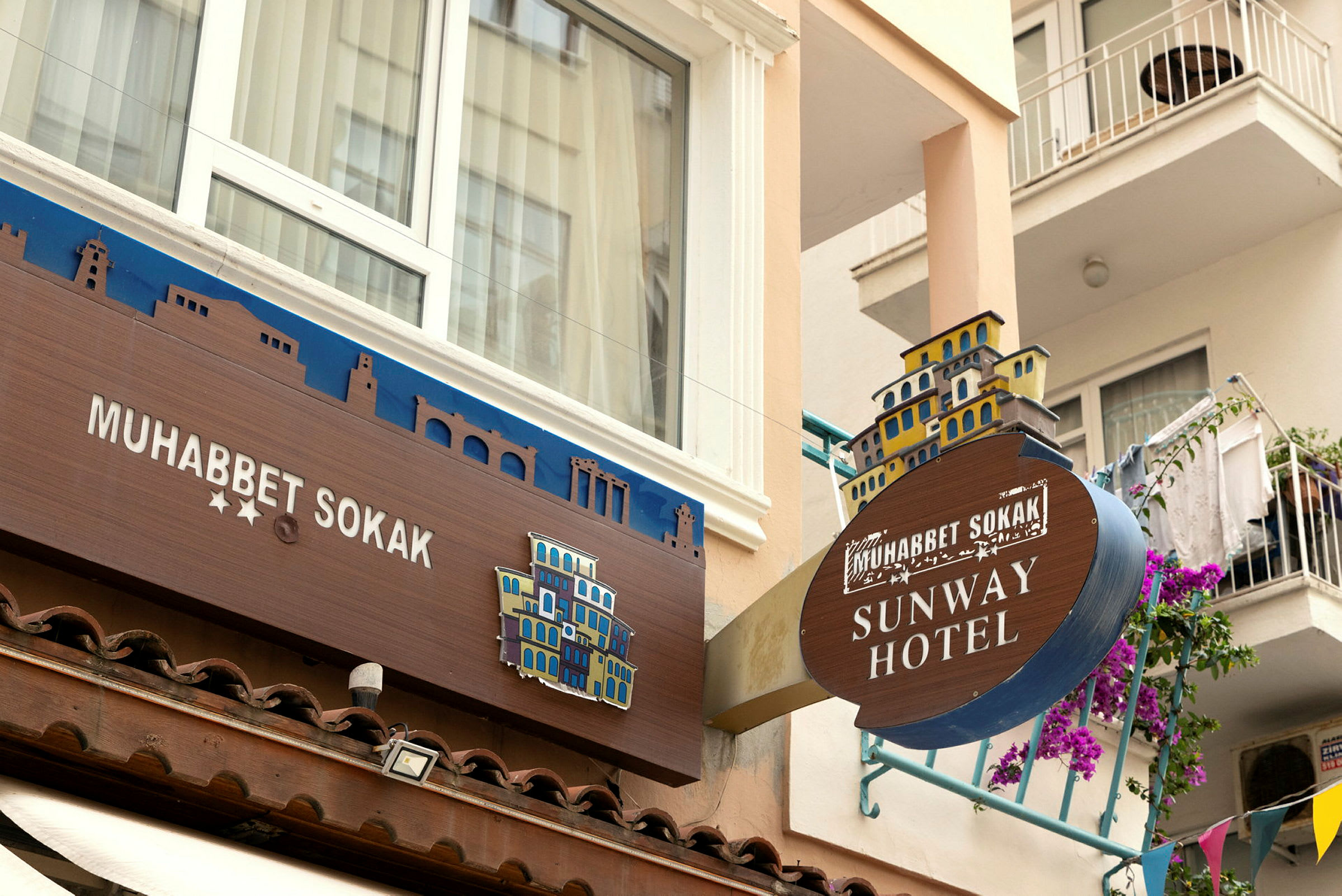 Bilde av fasaden til et hotell med skilt som viser navnene 'Muhabbet Sokak' og 'Sunway Hotel'. (AI-generert tekst)