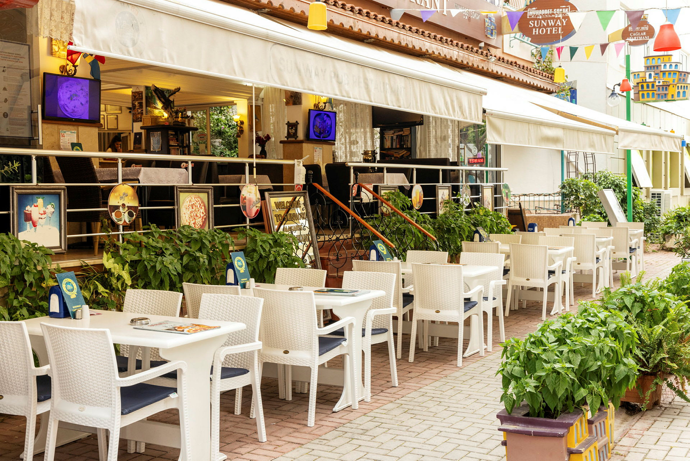 Restaurant med uteservering med hvite bord og stoler ved et hotell. (AI-generert tekst)