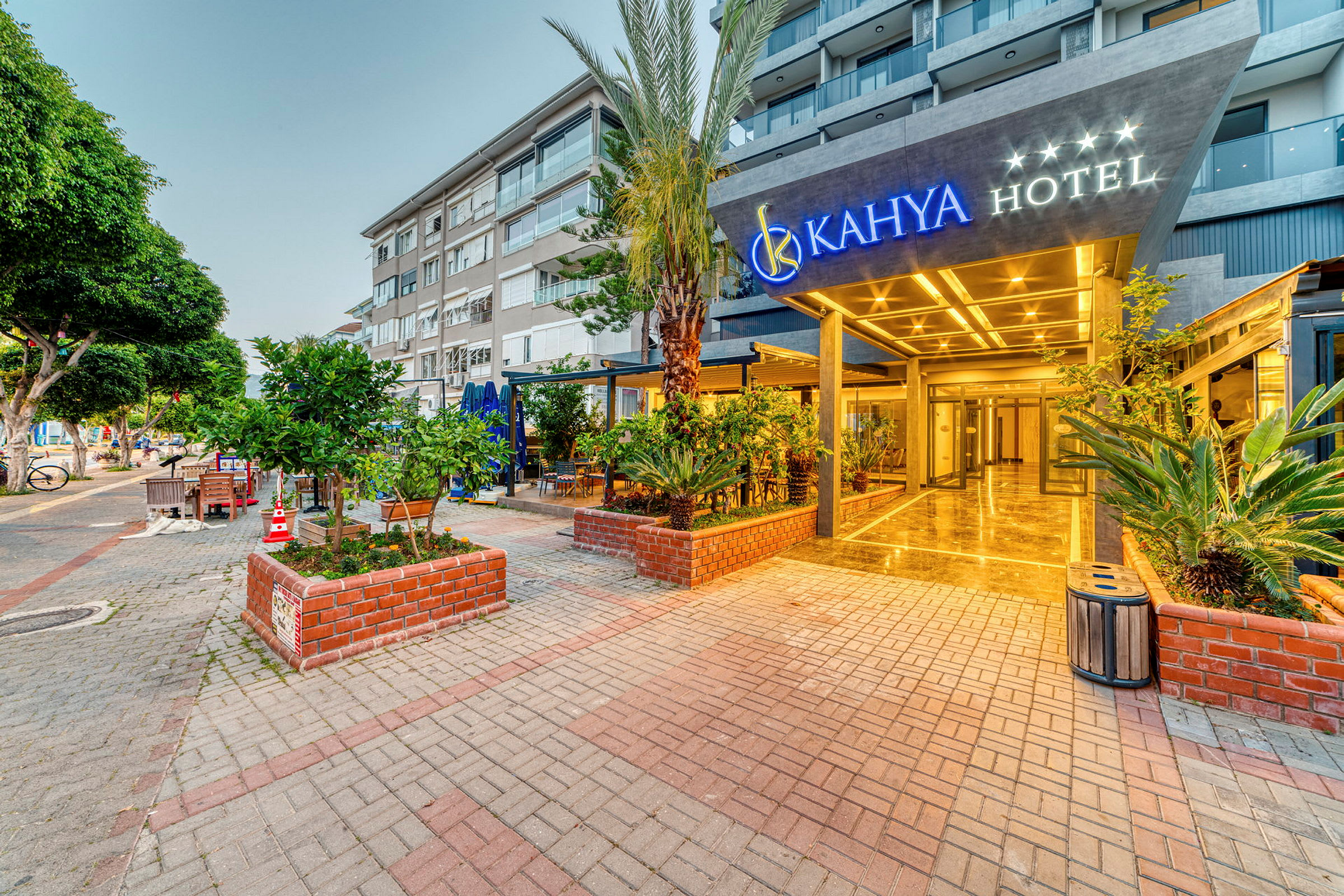 Inngangen til Kahya Hotel med omgivende frodige beplantninger og moderne bygninger i bakgrunnen. (AI-generert tekst)