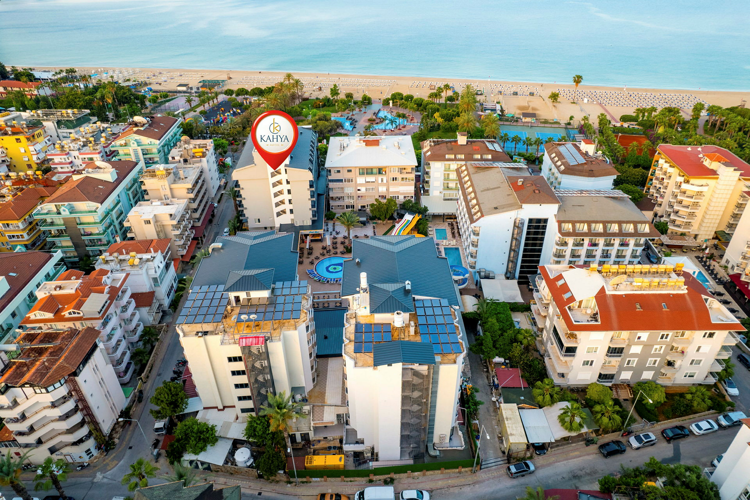 Flyfoto av et byområde ved stranden med flere bygninger, et basseng og bygningen markert som Kahya Hotel. (AI-generert tekst)