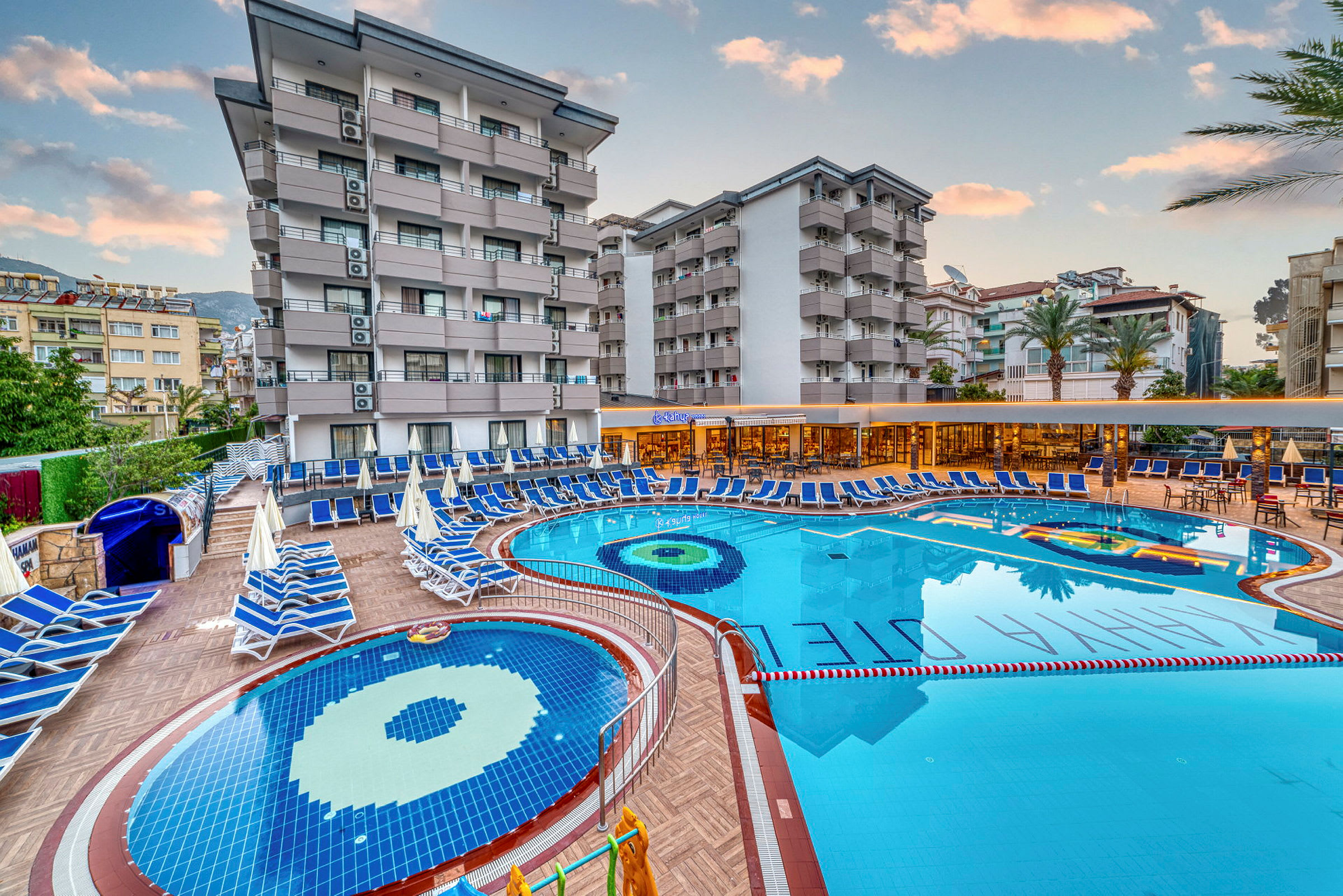 Hotellområde med bassenger, solsenger og bygninger i bakgrunnen. (AI-generert tekst)