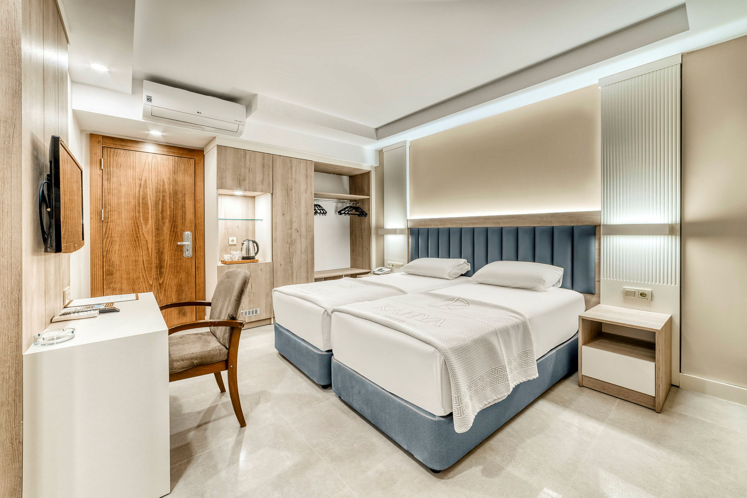Et hotellrom med to enkeltsenger, skrivebord, stol og garderobe. (AI-generert tekst)