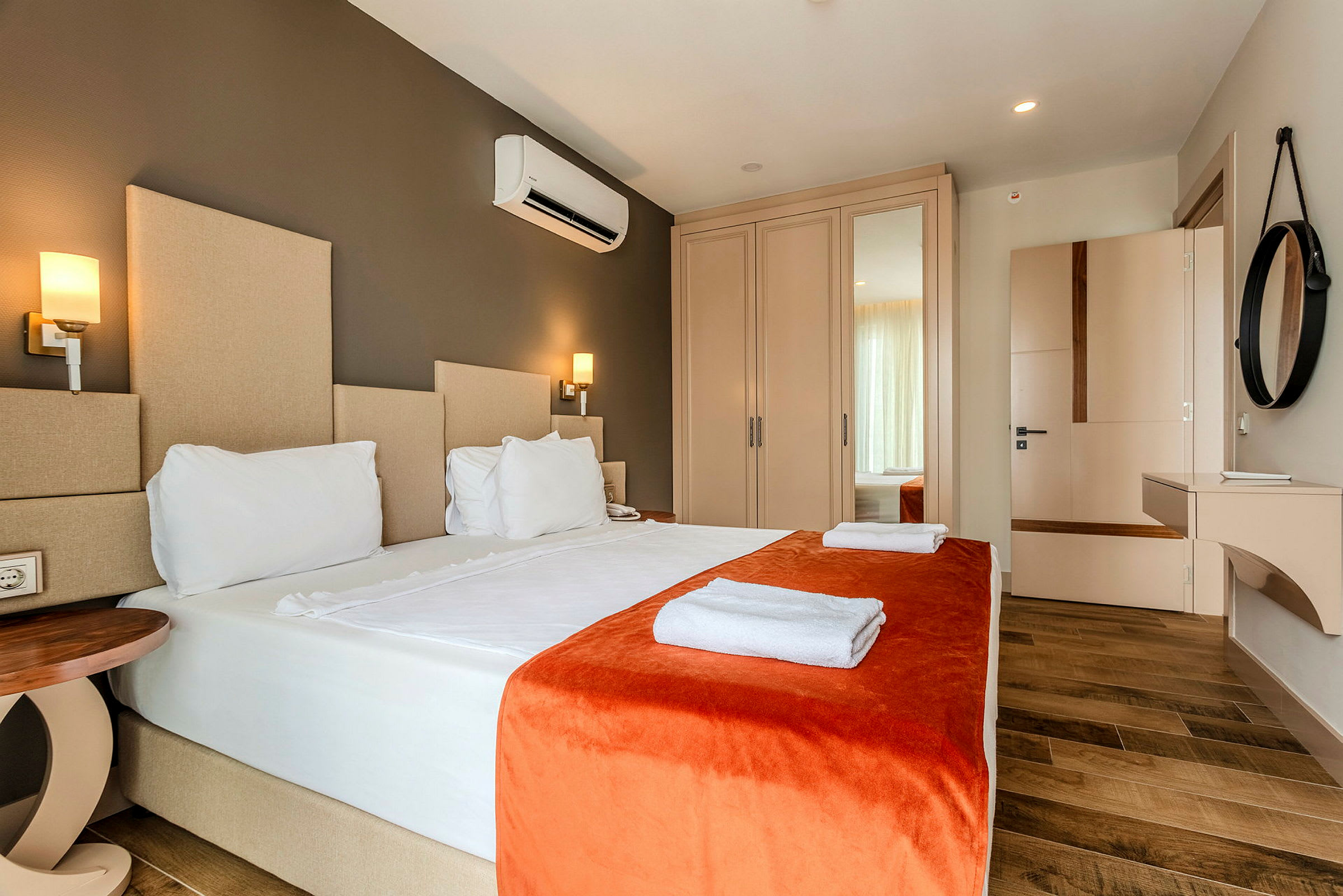Et hotellrom med en dobbeltseng kledd i hvite laken og oransje sengeteppe, med håndklær plassert på sengen. (AI-generert tekst)