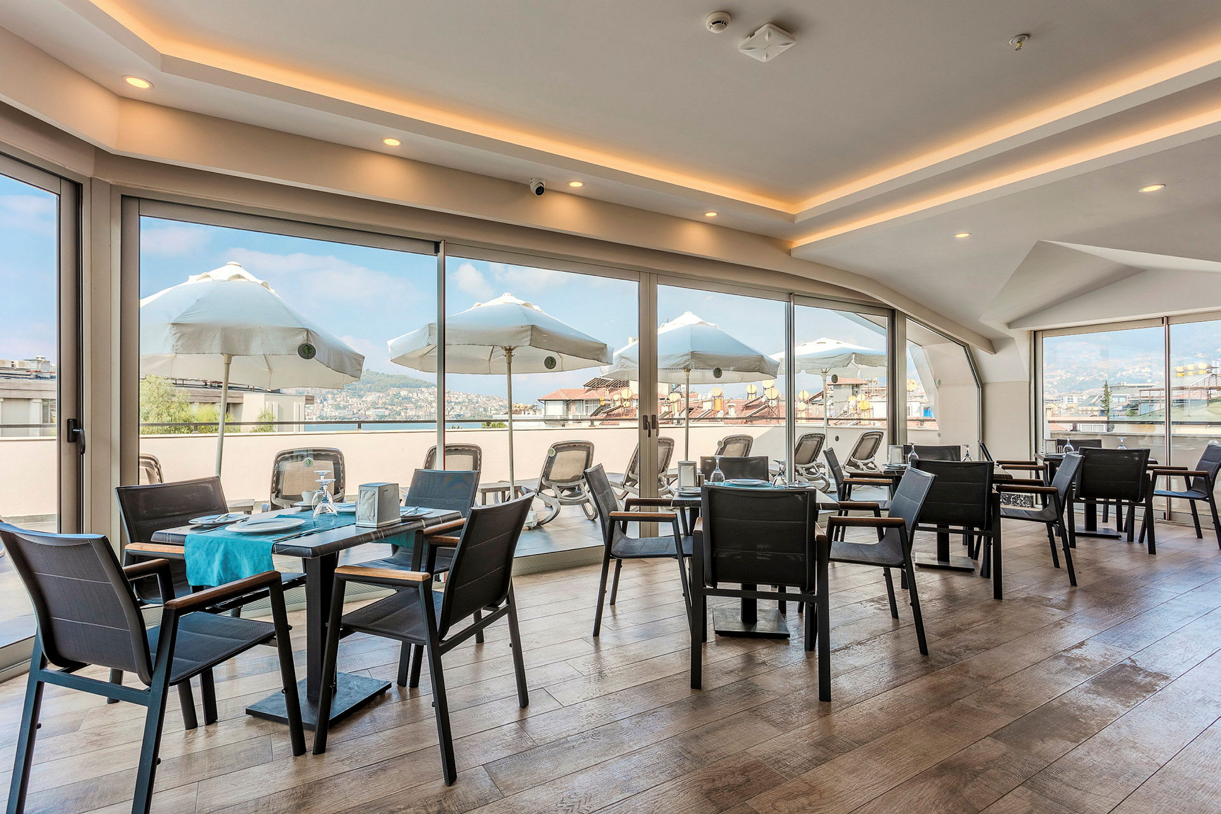 En restaurant med glassvegger og utsikt mot solparasoller og omgivelser. (AI-generert tekst)