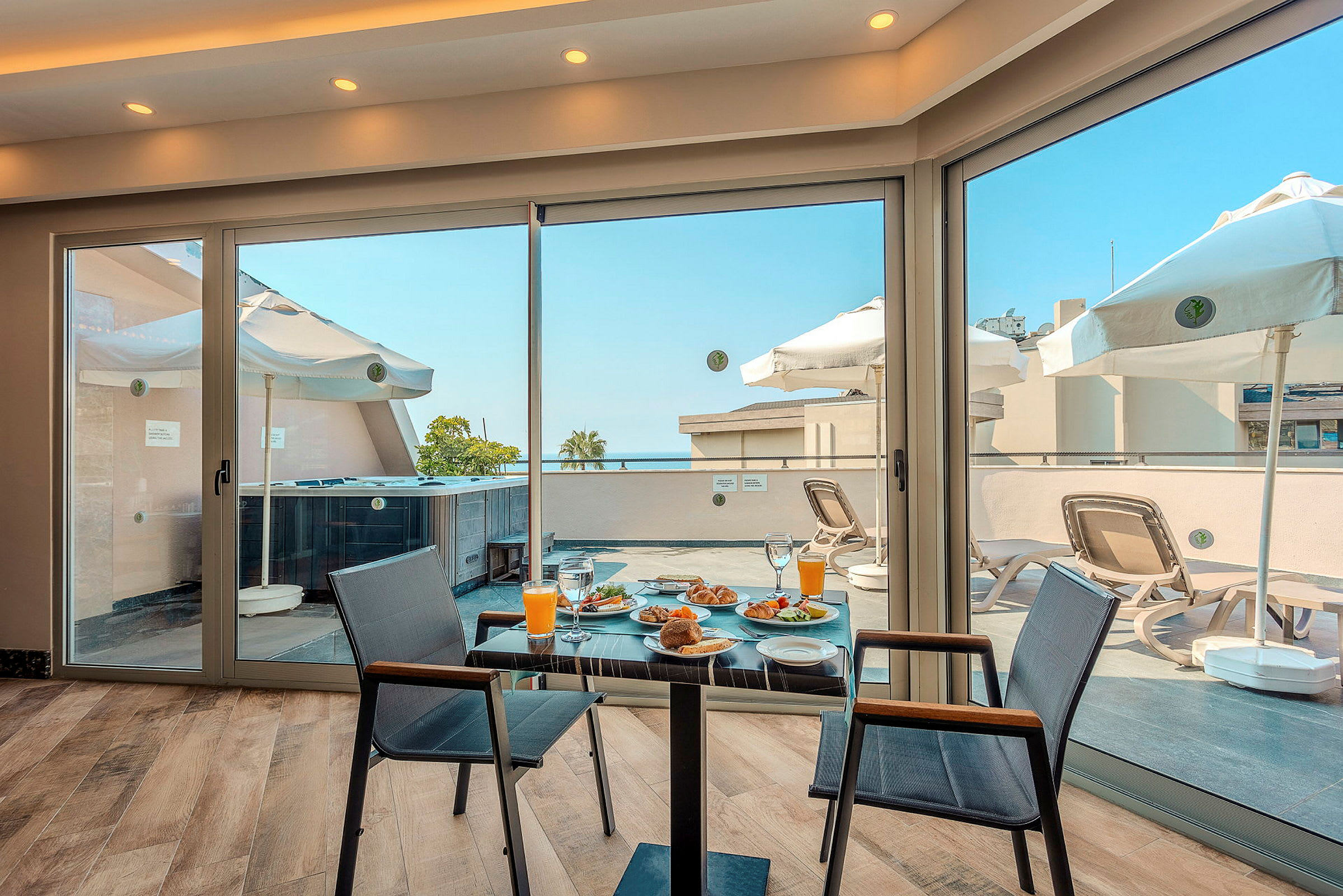 Utsikt fra et rom med frokost på et bord og en terrasse med solsenger og parasoller. (AI-generert tekst)