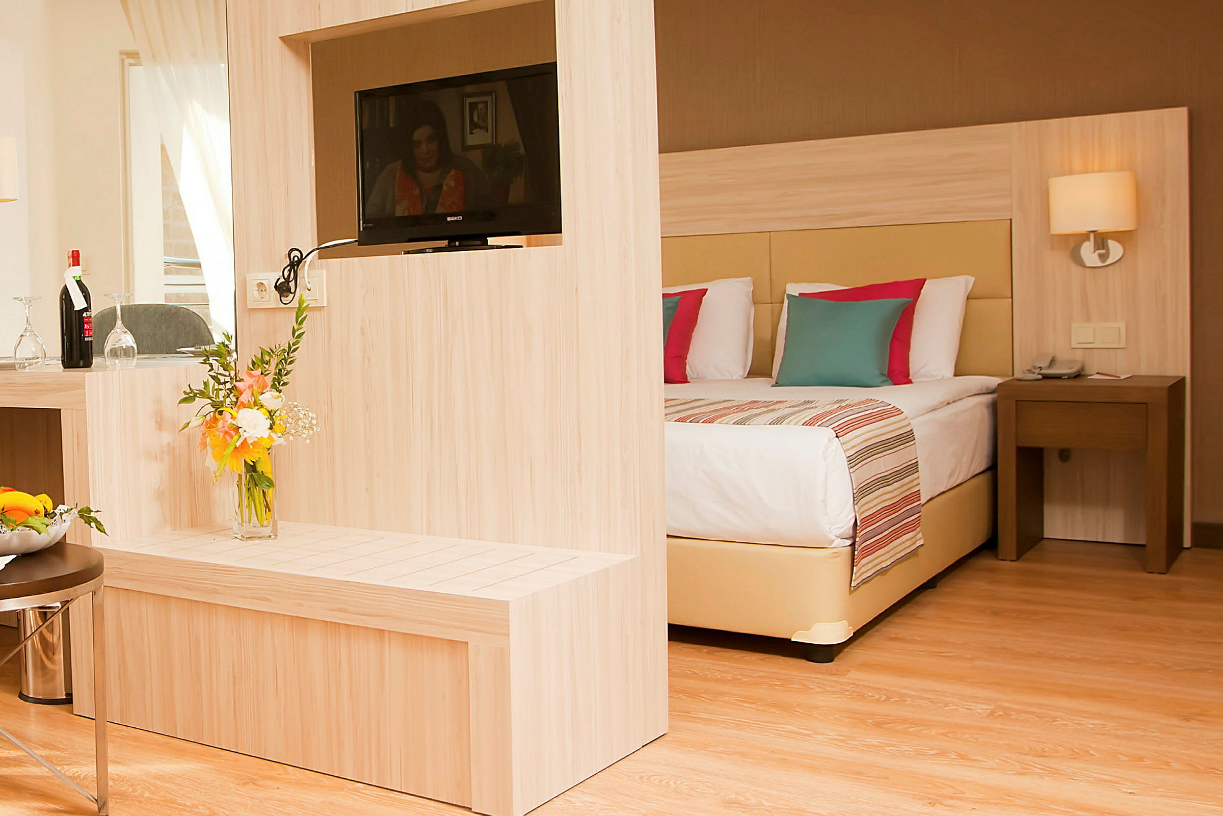 Et hotellrom med moderne innredning, inkludert en dobbeltseng, en TV på en trebjelke og en blomsterbukett. (AI-generert tekst)