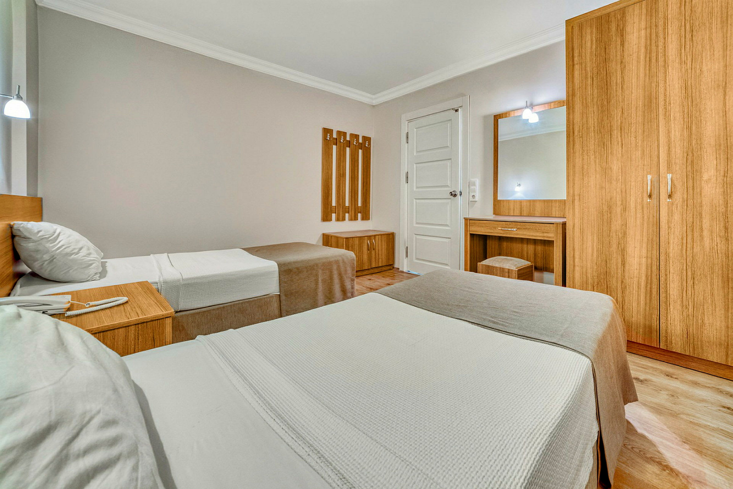 Interiør i et hotellrom med to enkeltsenger, treskap og sminkebord. (AI-generert tekst)