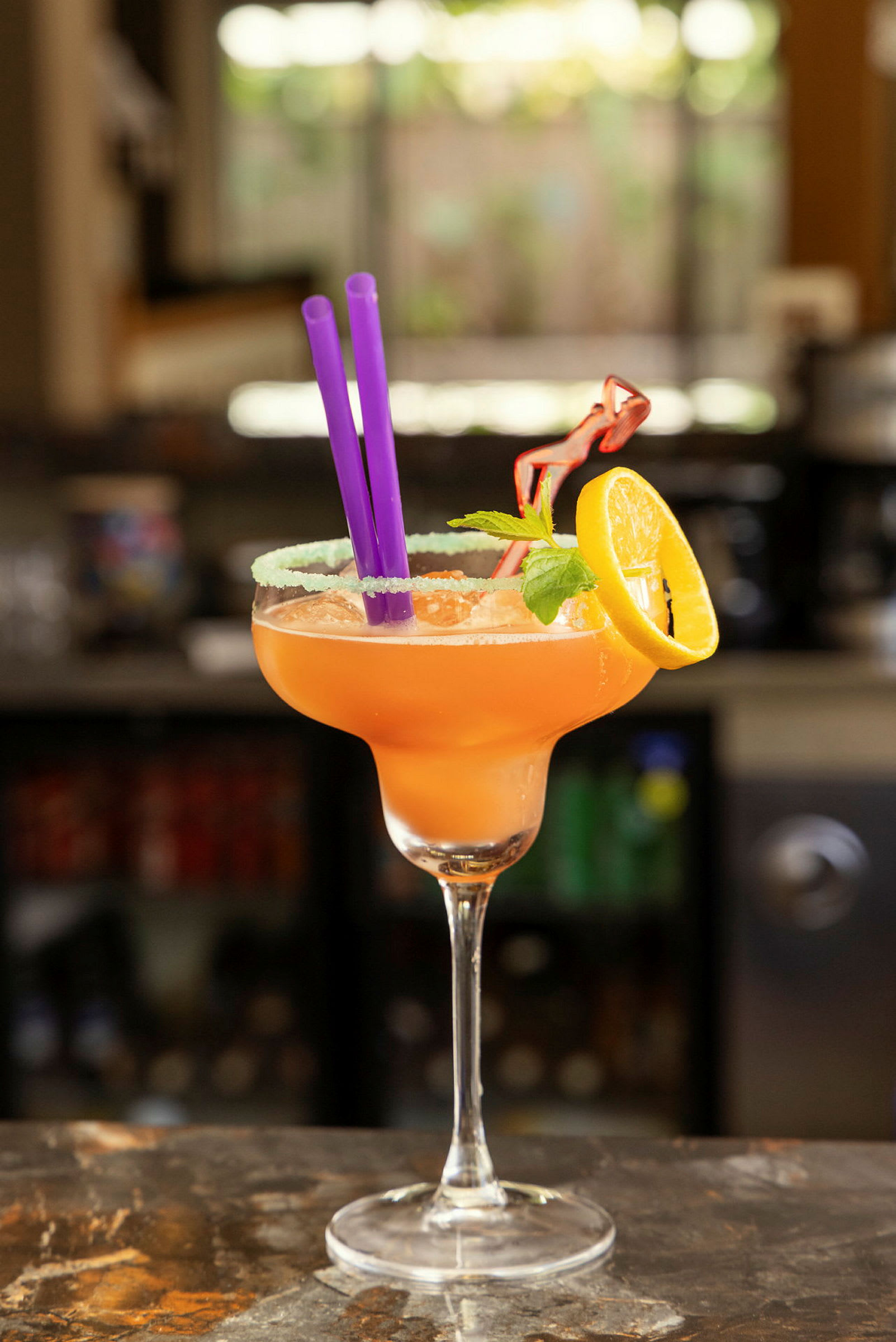 En cocktail servert i et glass med en sitronskive, mynteblader og sugerør. (AI-generert tekst)