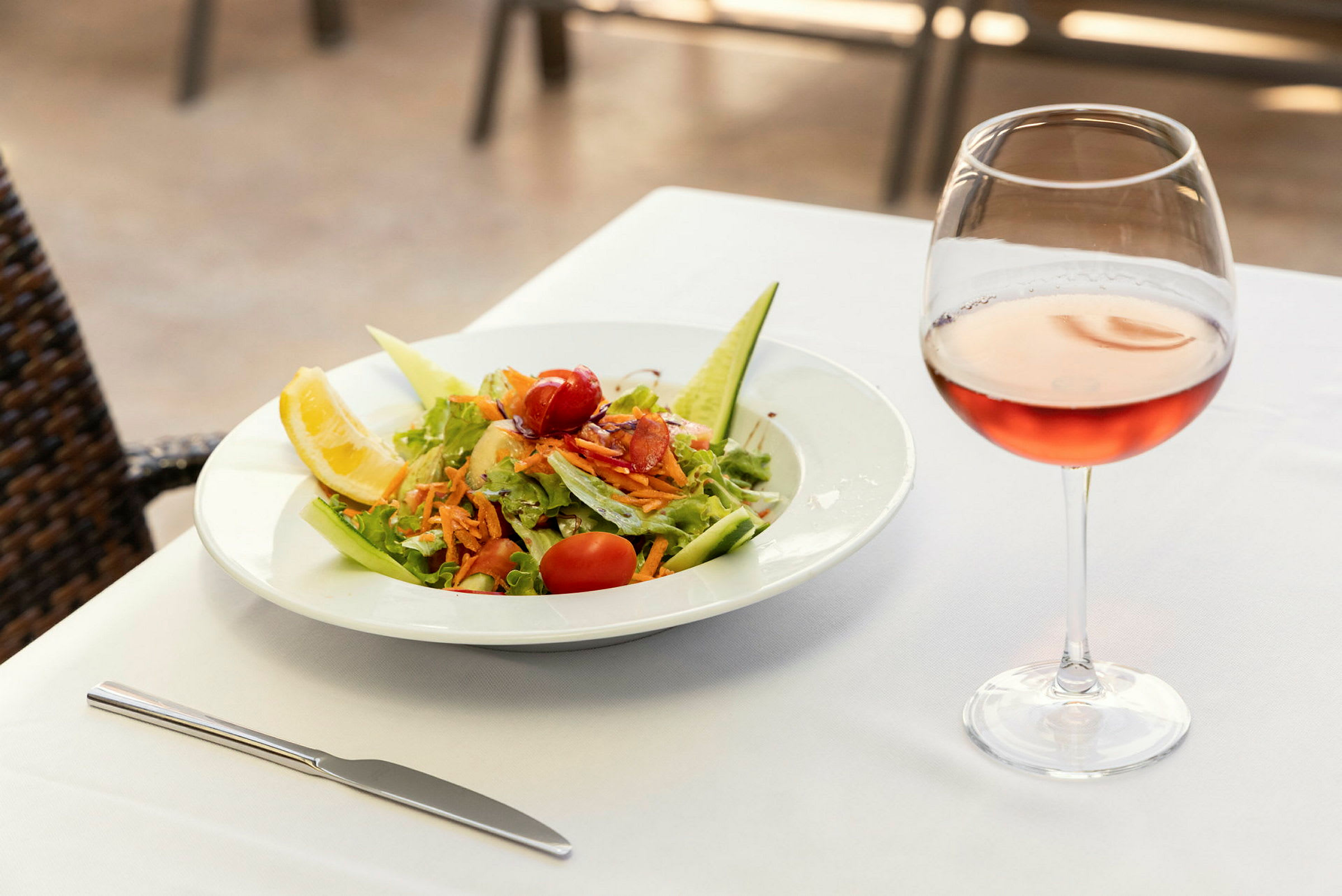 En tallerken med salat og et glass rosévin på et dekket bord. (AI-generert tekst)
