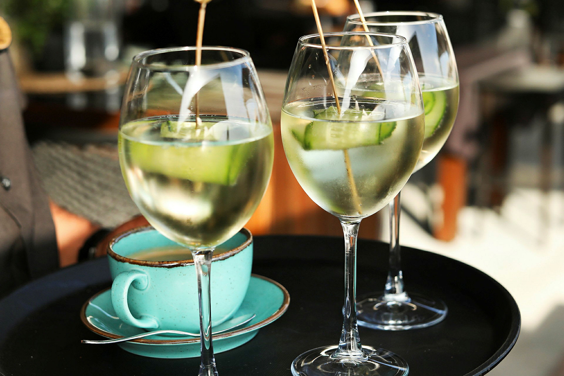 Tre glass med drikke som inneholder isbiter og agurkskiver, samt en turkis kaffekopp på en serveringsbrett. (AI-generert tekst)