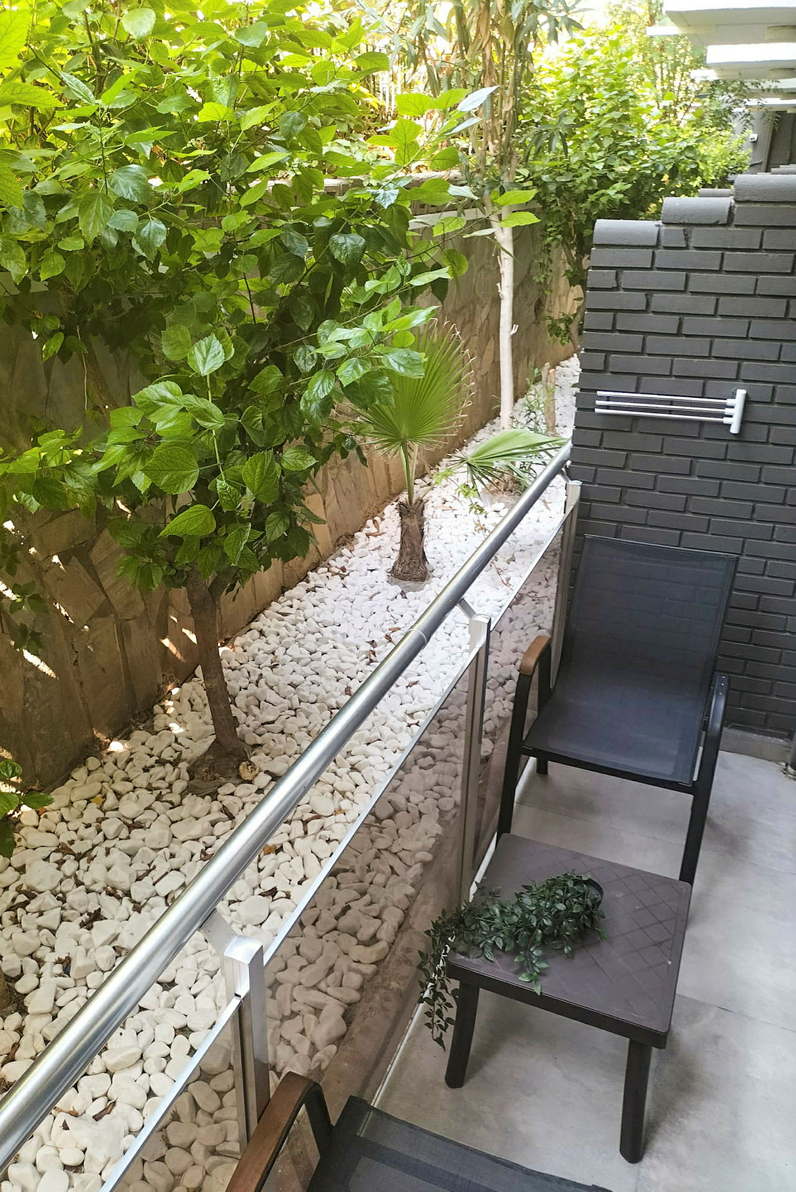 En liten uteplass med to stoler og et bord, med grønne planter og steinlegging ved siden av. (AI-generert tekst)