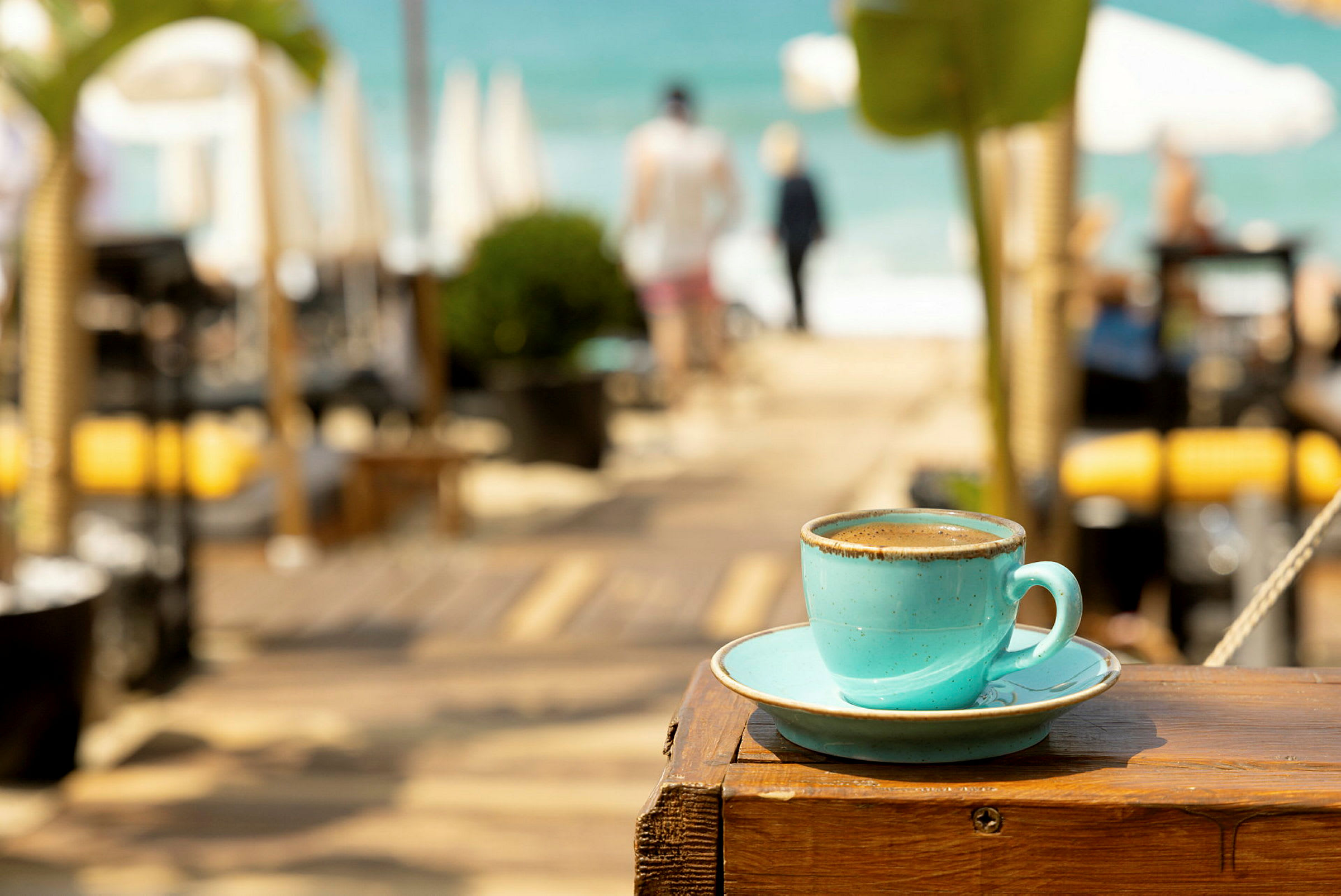 En kopp kaffe på en treflate med en strand i bakgrunnen. (AI-generert tekst)