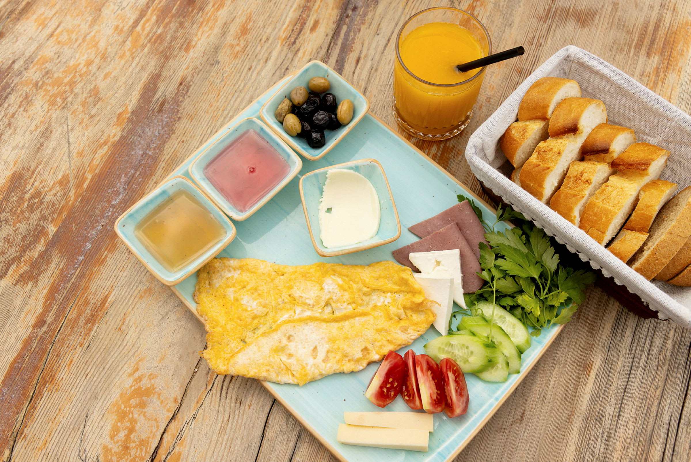En frokost med omelett, grønnsaker, ost, brød, oliven og appelsinjuice. (AI-generert tekst)