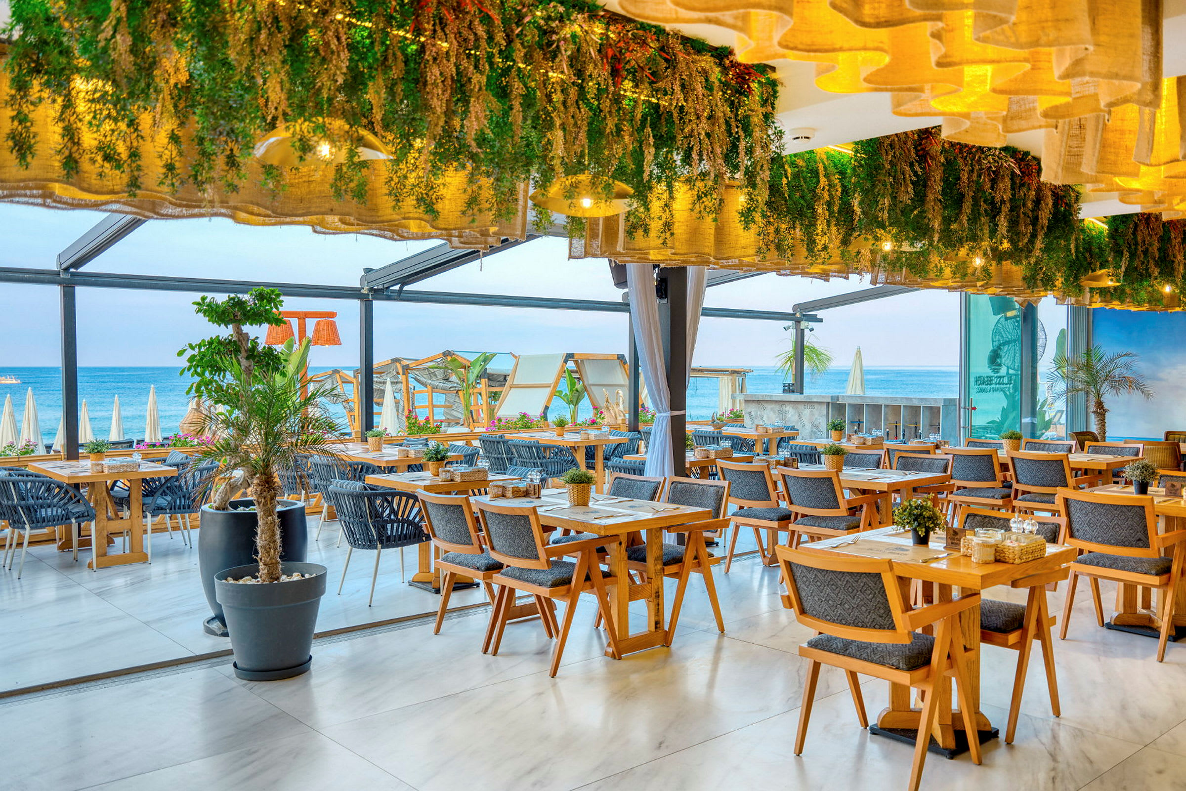 Restaurant med trebord, dekorative planter og utsikt mot stranden. (AI-generert tekst)