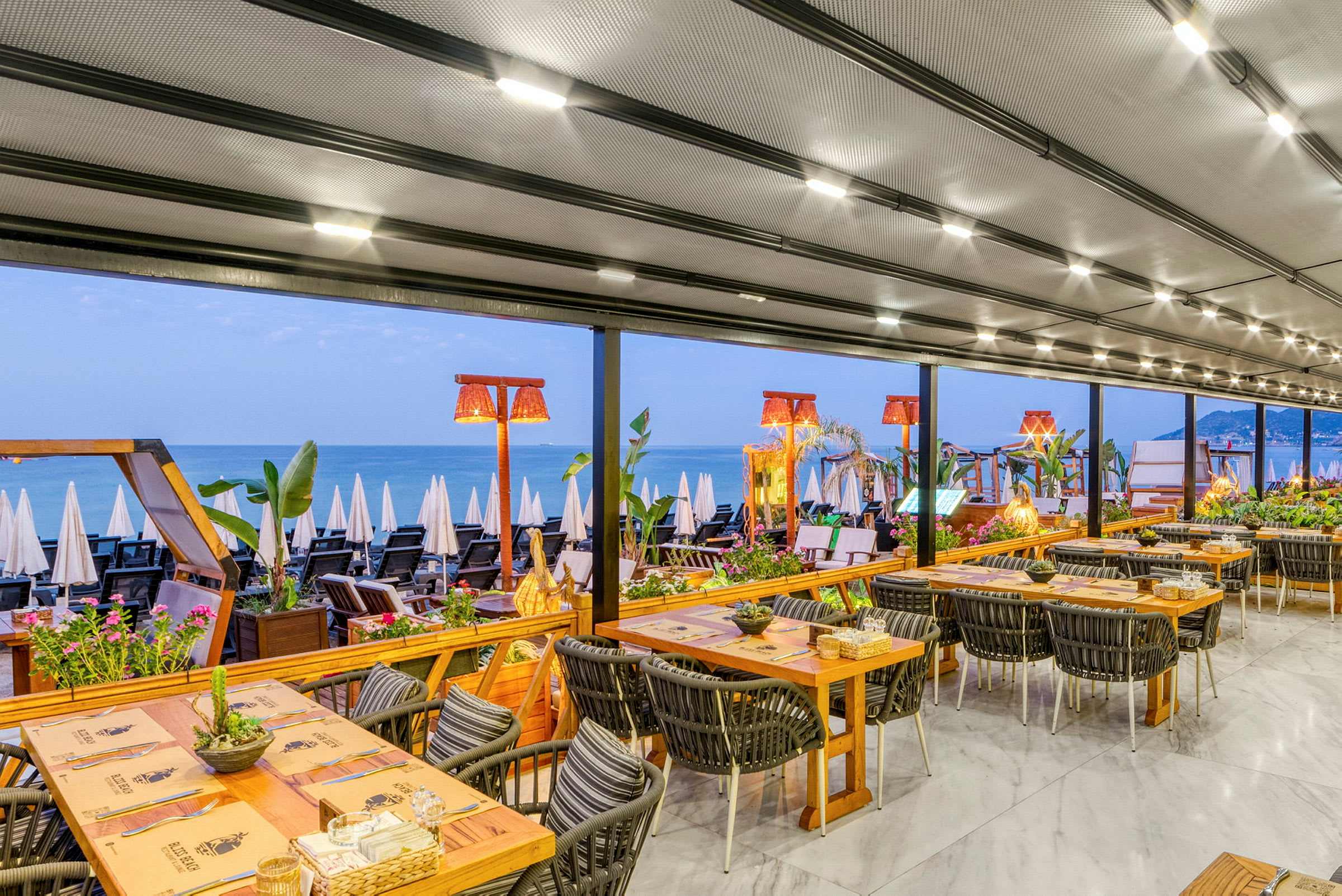 En restaurant med utsikt mot en strand og havet, bordene er dekket til måltid. (AI-generert tekst)