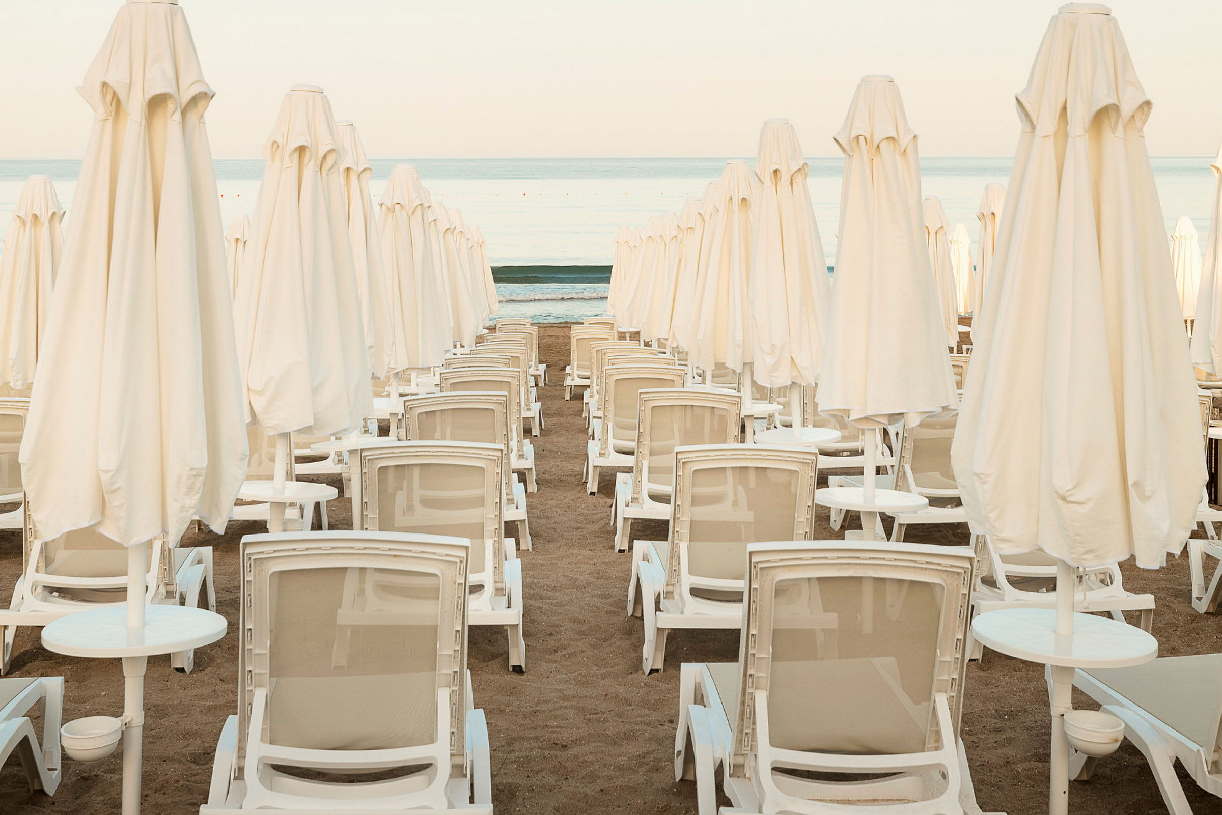 Flere solsenger og strandparasoller på rad på sandstrand. (AI-generert tekst)
