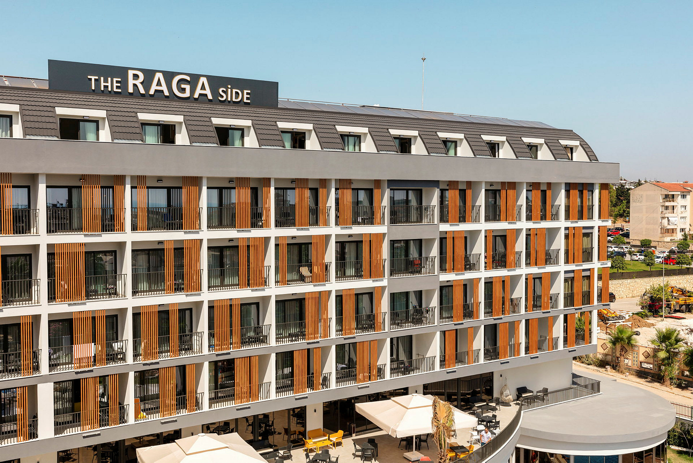 Hotellkompleks med flere etasjer med balkonger og et skilt som viser navnet 'The RAGA Side'. (AI-generert tekst)