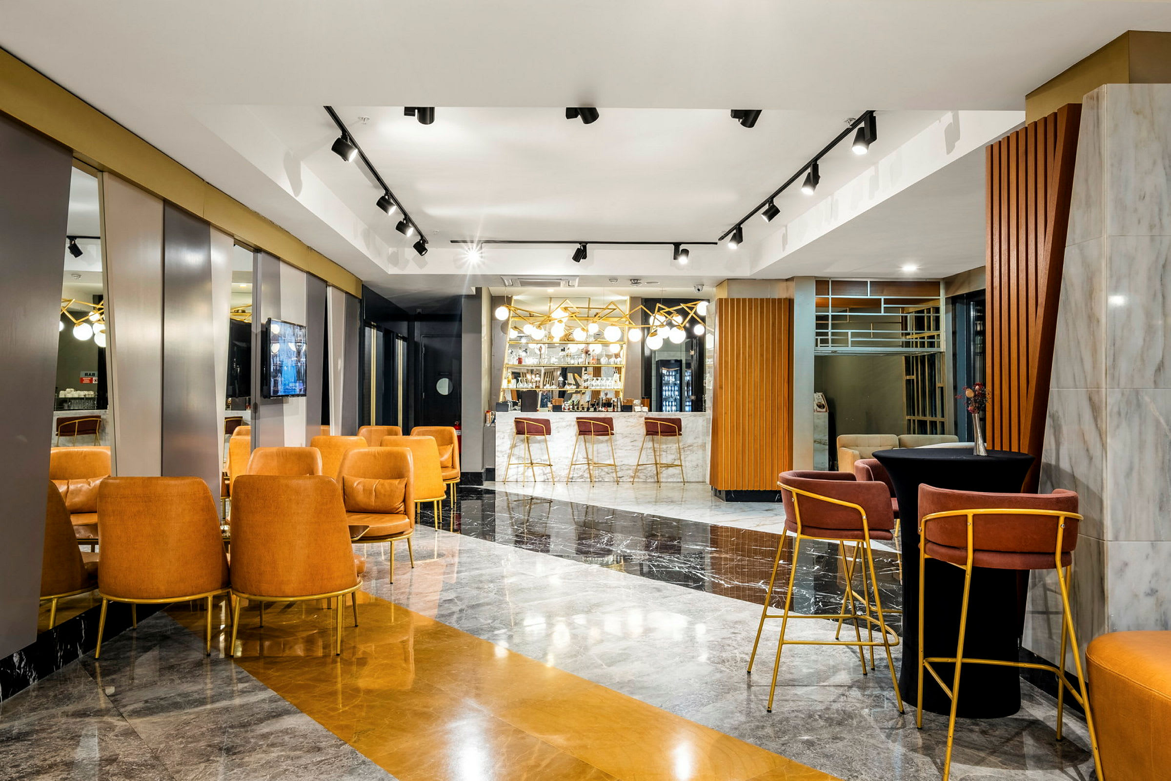 Interiøret viser en moderne lounge med sitteplasser, sofaer og en bar i bakgrunnen dekorert med lysekroner og speil. (AI-generert tekst)