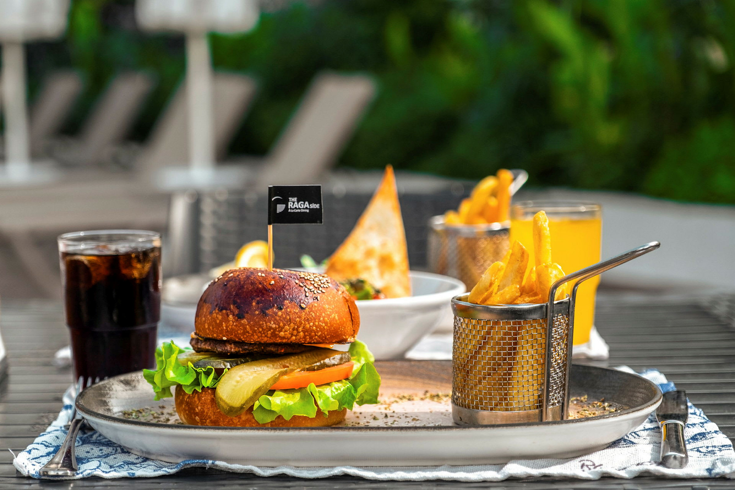 En tallerken med en hamburger, pommes frites og drikke utendørs. (AI-generert tekst)
