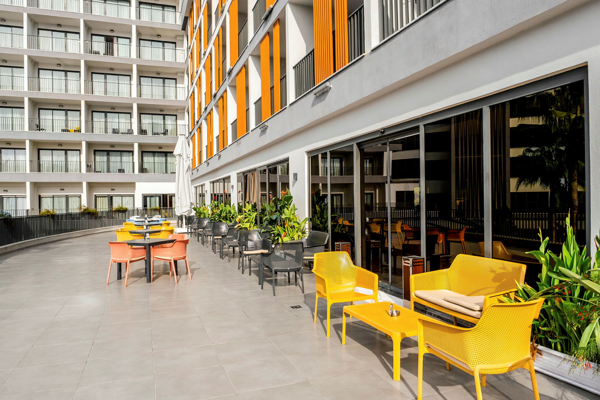 Utendørs serveringsområde med fargerike stoler og et moderne hotell i bakgrunnen. (AI-generert tekst)