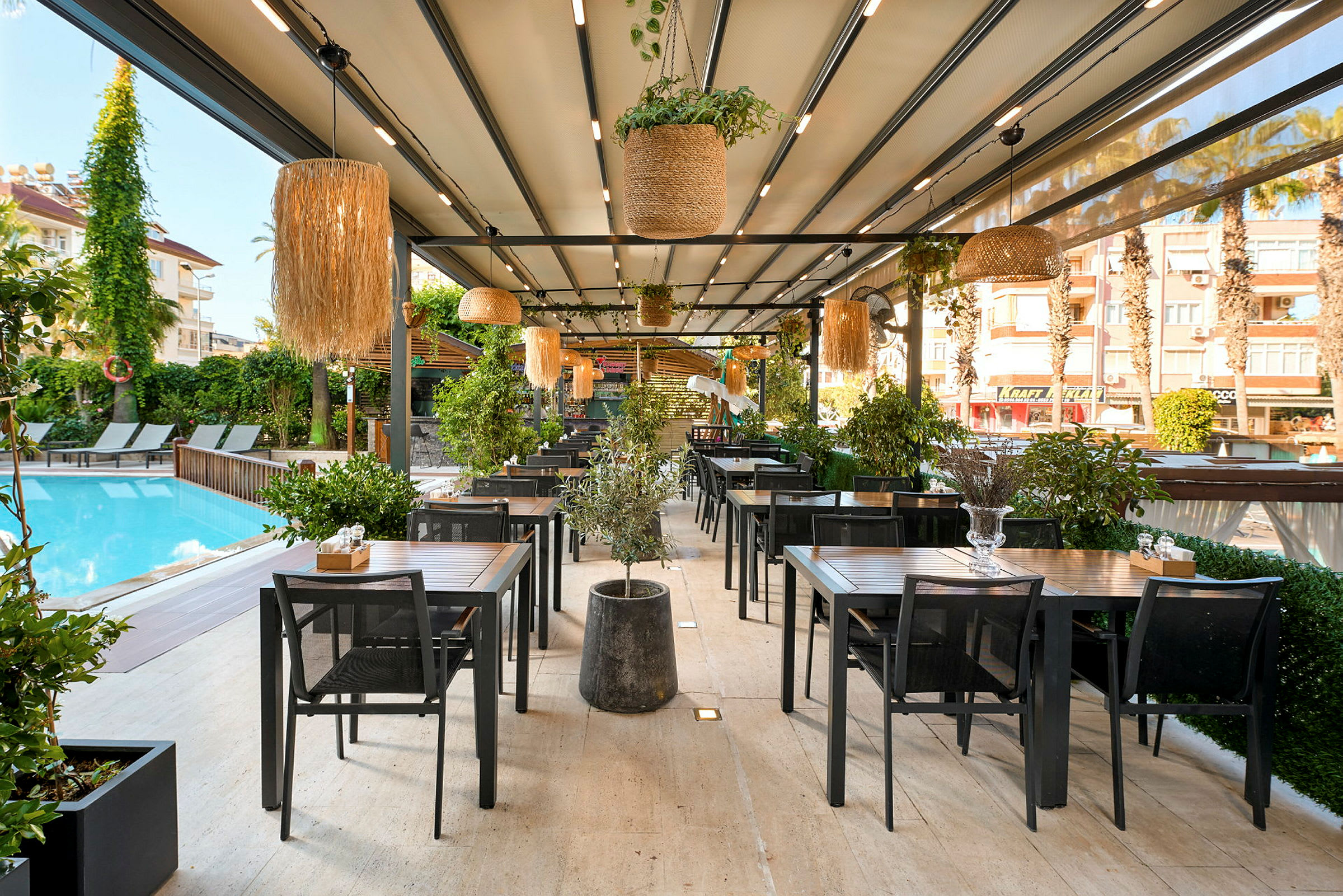 Utendørsrestaurant ved et basseng med bord og stoler samt grønne planter. (AI-generert tekst)