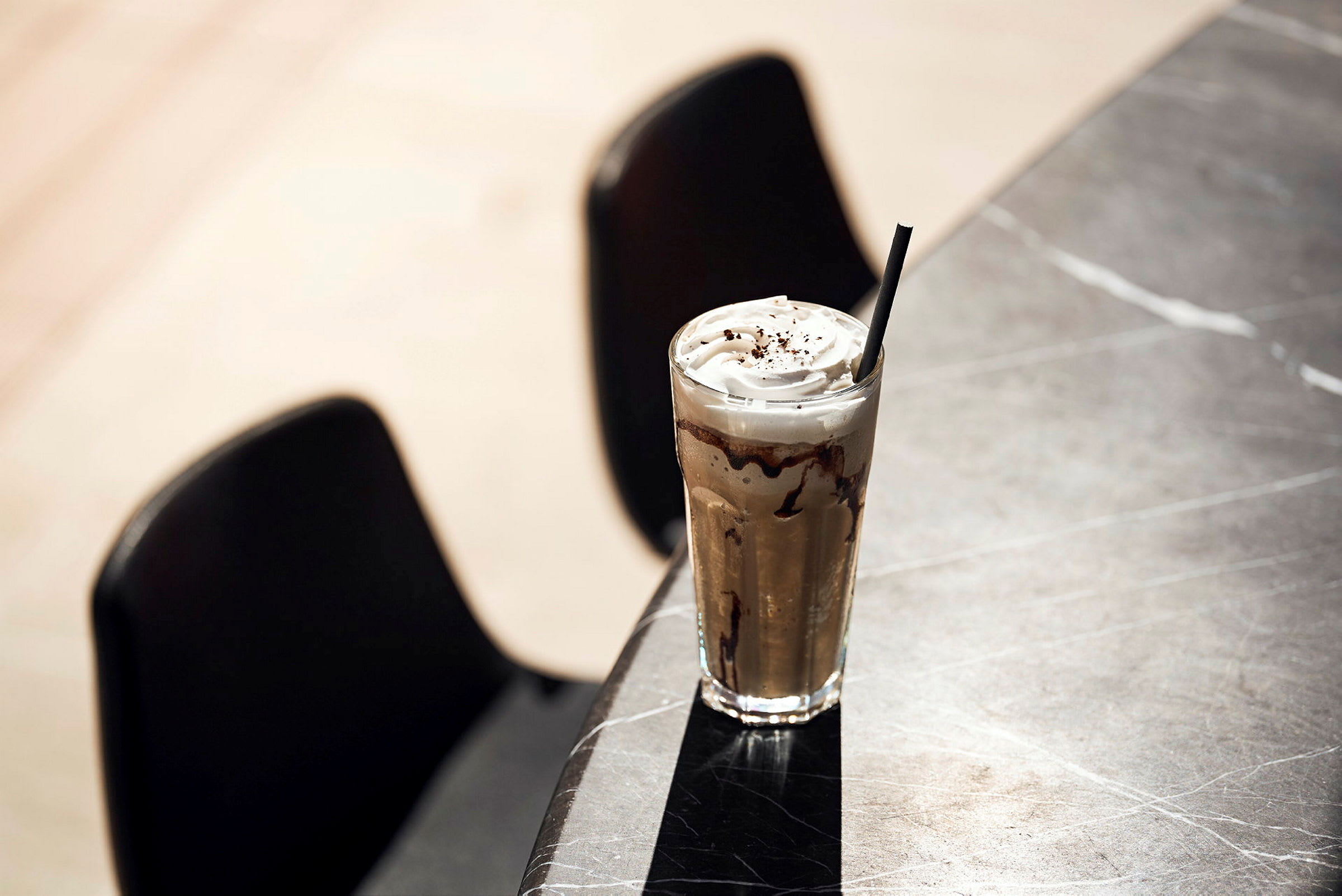 Et glass iskaffe med krem og sjokolade pynter et bord. (AI-generert tekst)