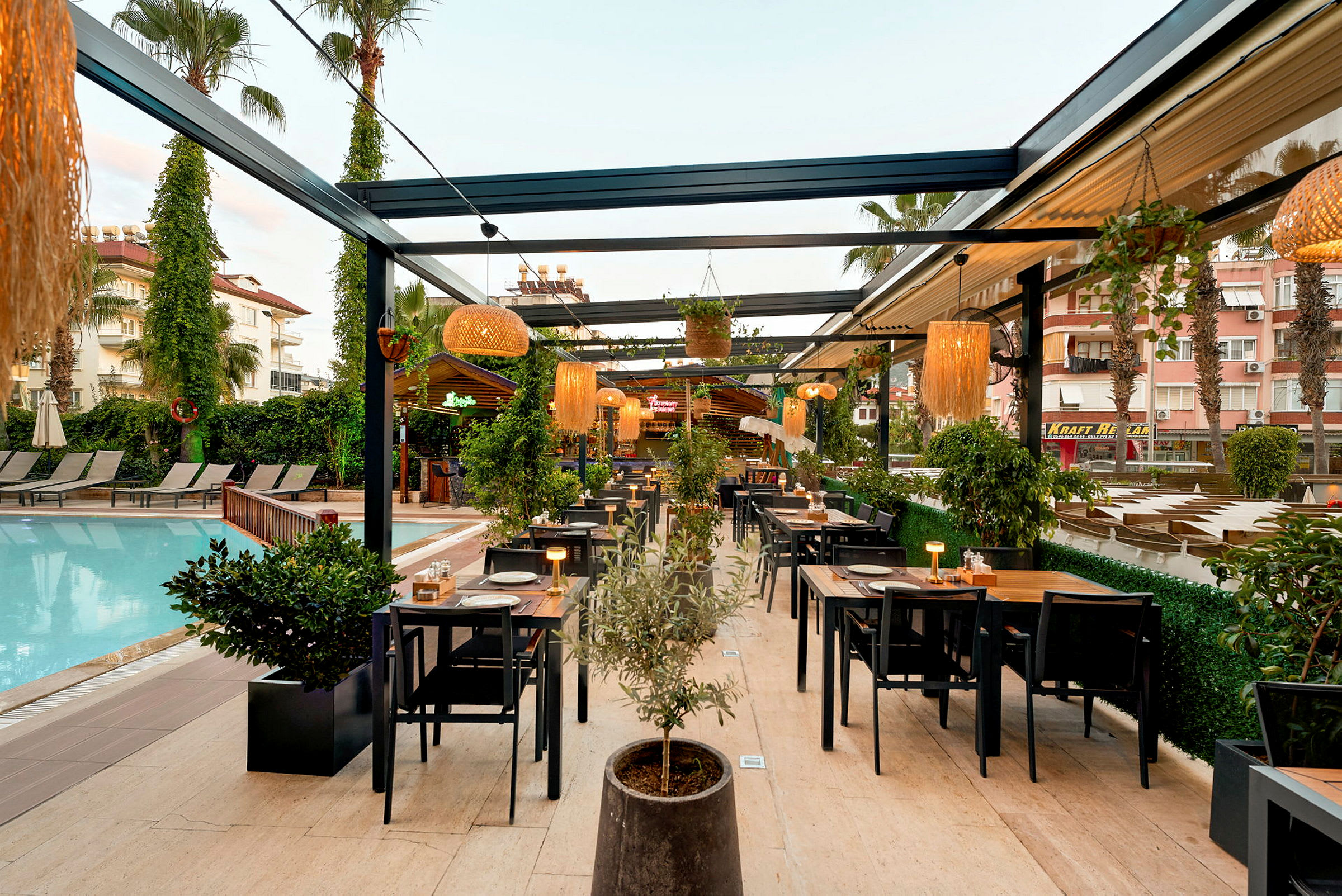 Utendørsrestaurant ved et basseng med bord og stoler samt planter og belysning. (AI-generert tekst)